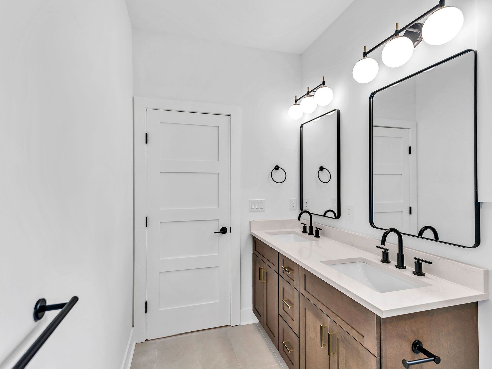 Bathroom with double vanity, black fixtures, white countertop, and light wood cabinets.