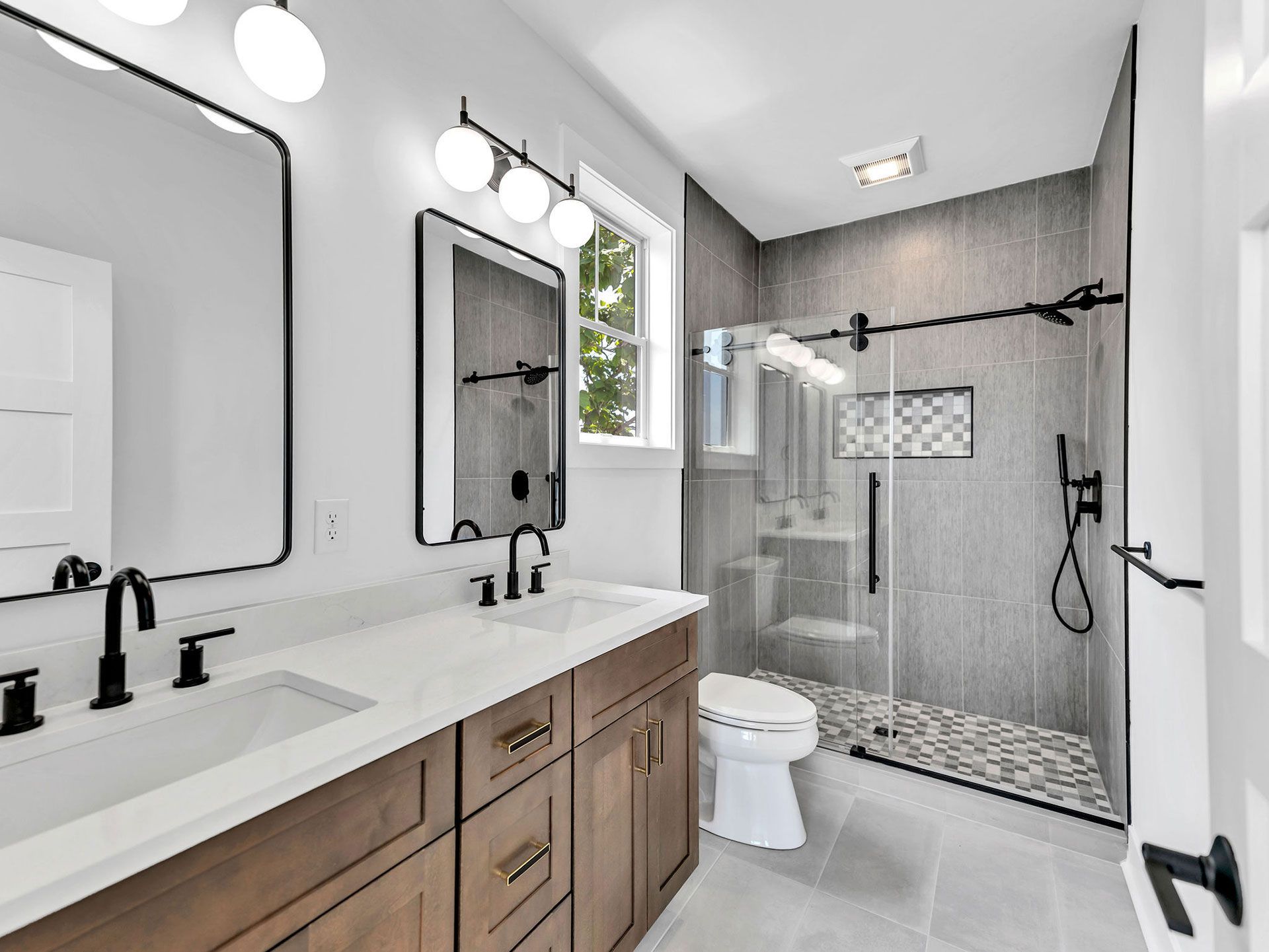 Bathroom with a double vanity, walk-in shower, and a toilet. Brown cabinetry with black fixtures.
