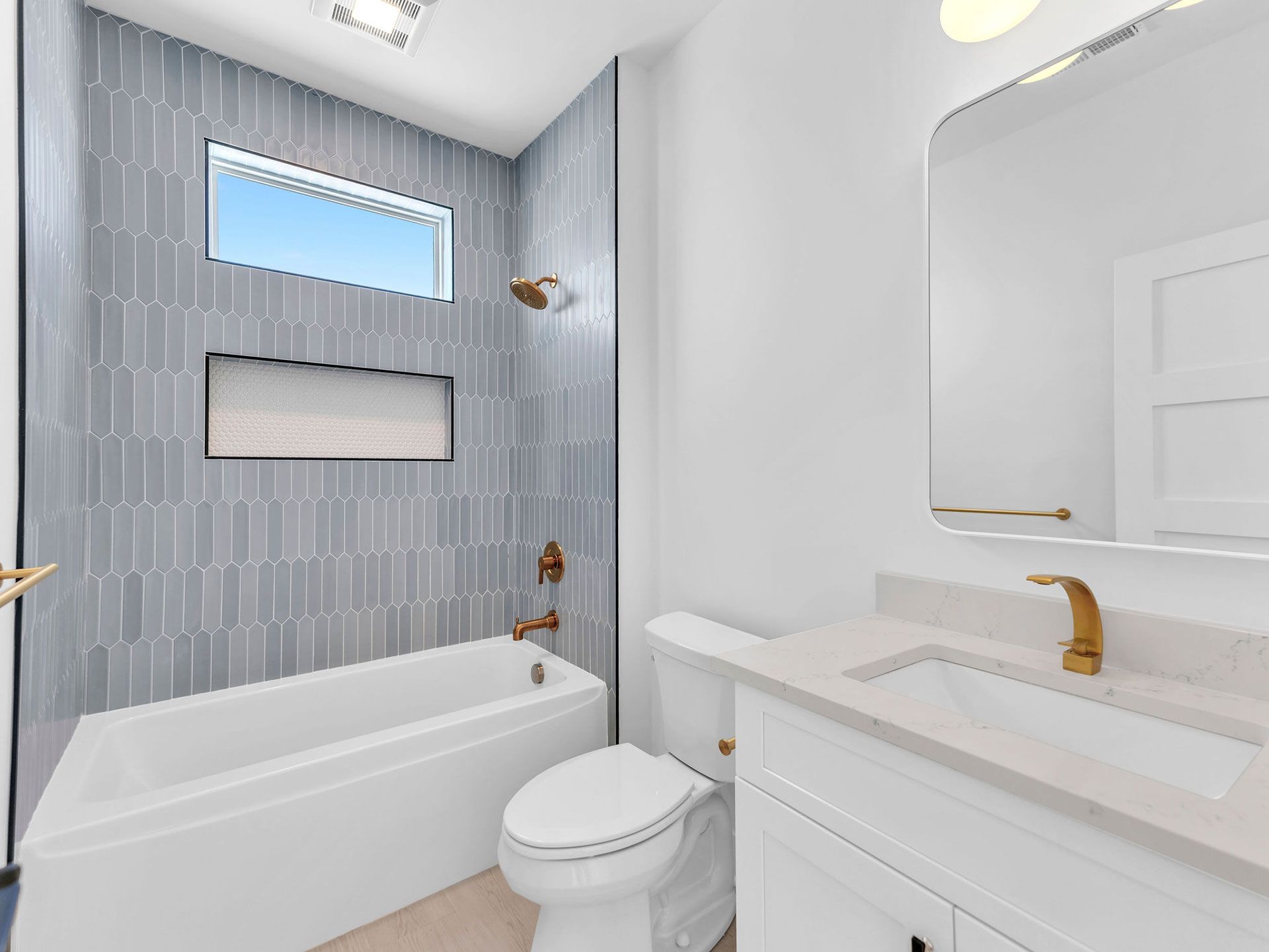 Bathroom with blue tiled accent wall, white tub, vanity, and toilet. Gold fixtures.