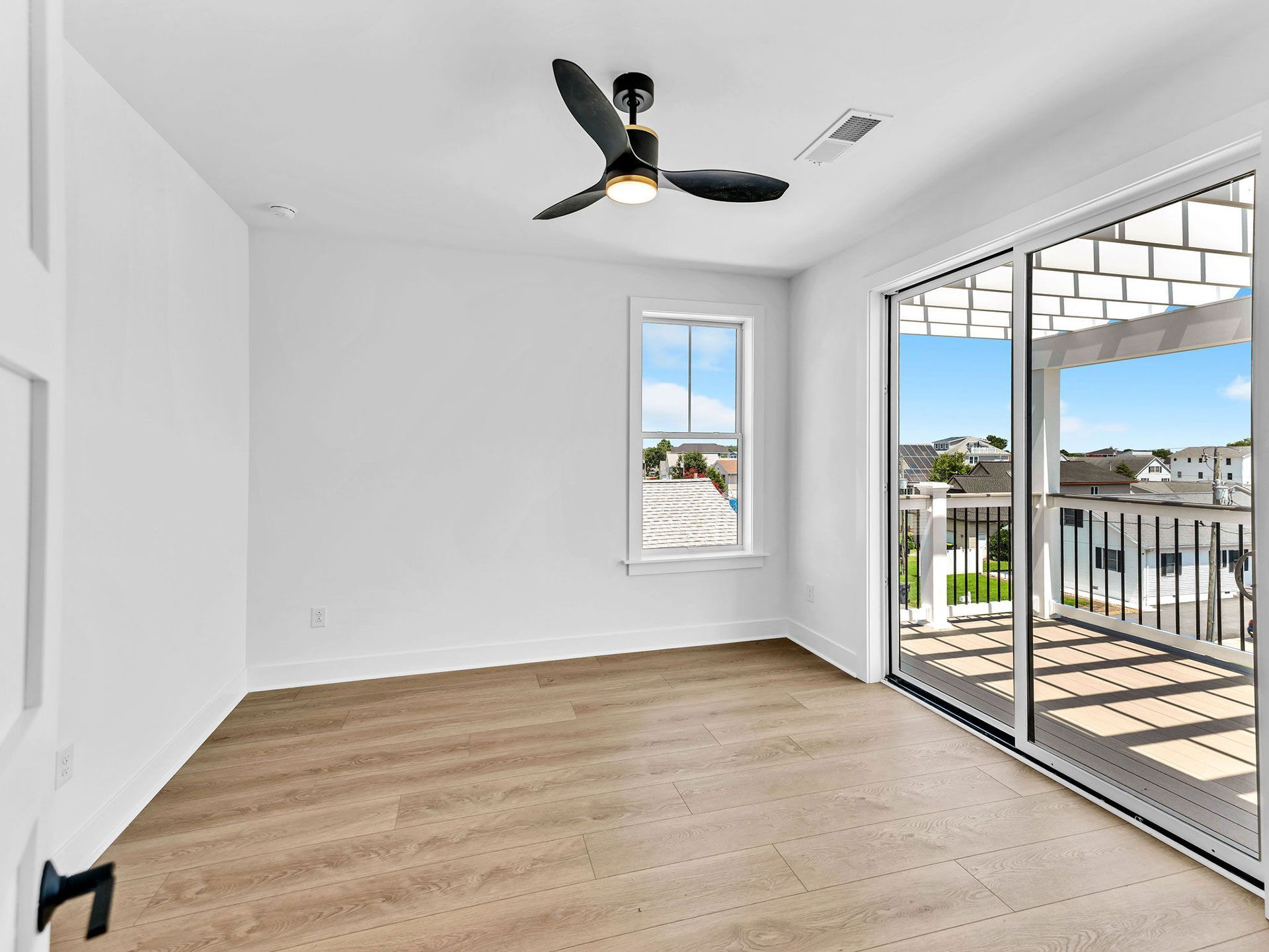 Empty bedroom with carpet, white walls, ceiling fan, window, and sliding door to a balcony with a view.