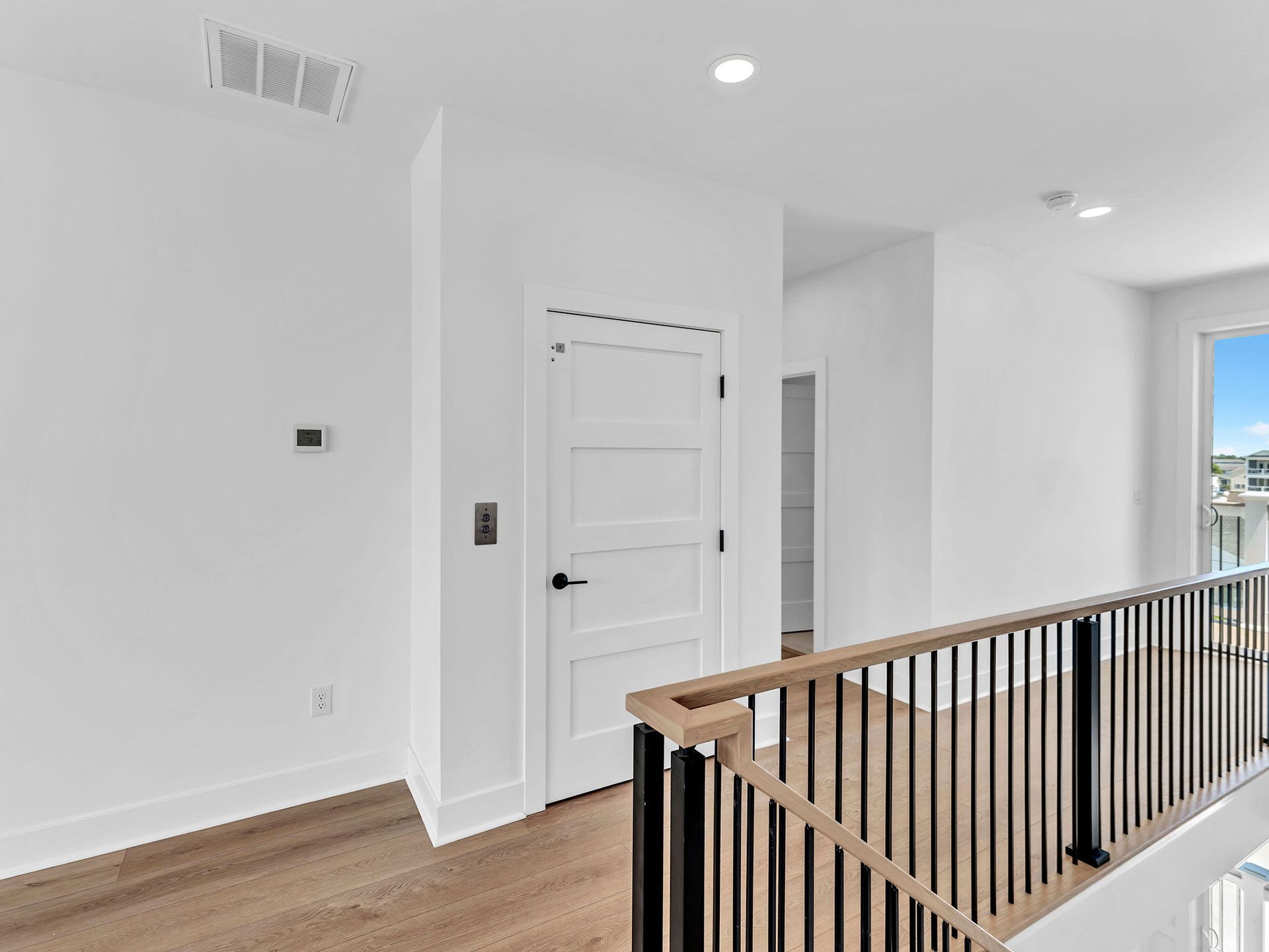 Interior view of a white hallway with wooden floor, door, and railing.