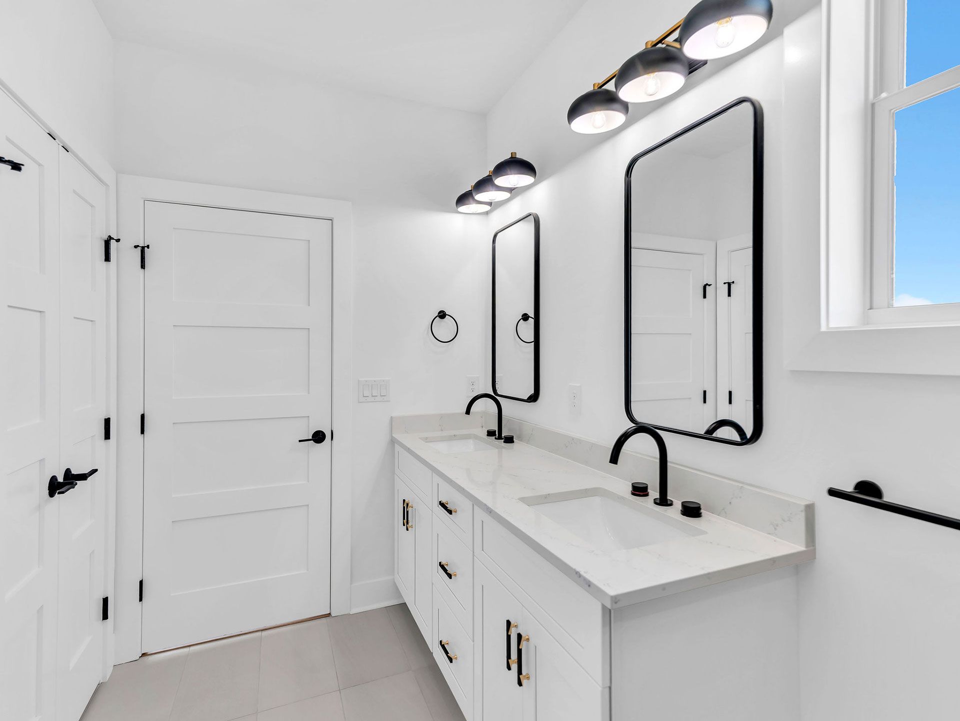 White bathroom with double vanity, black fixtures, and large mirrors.