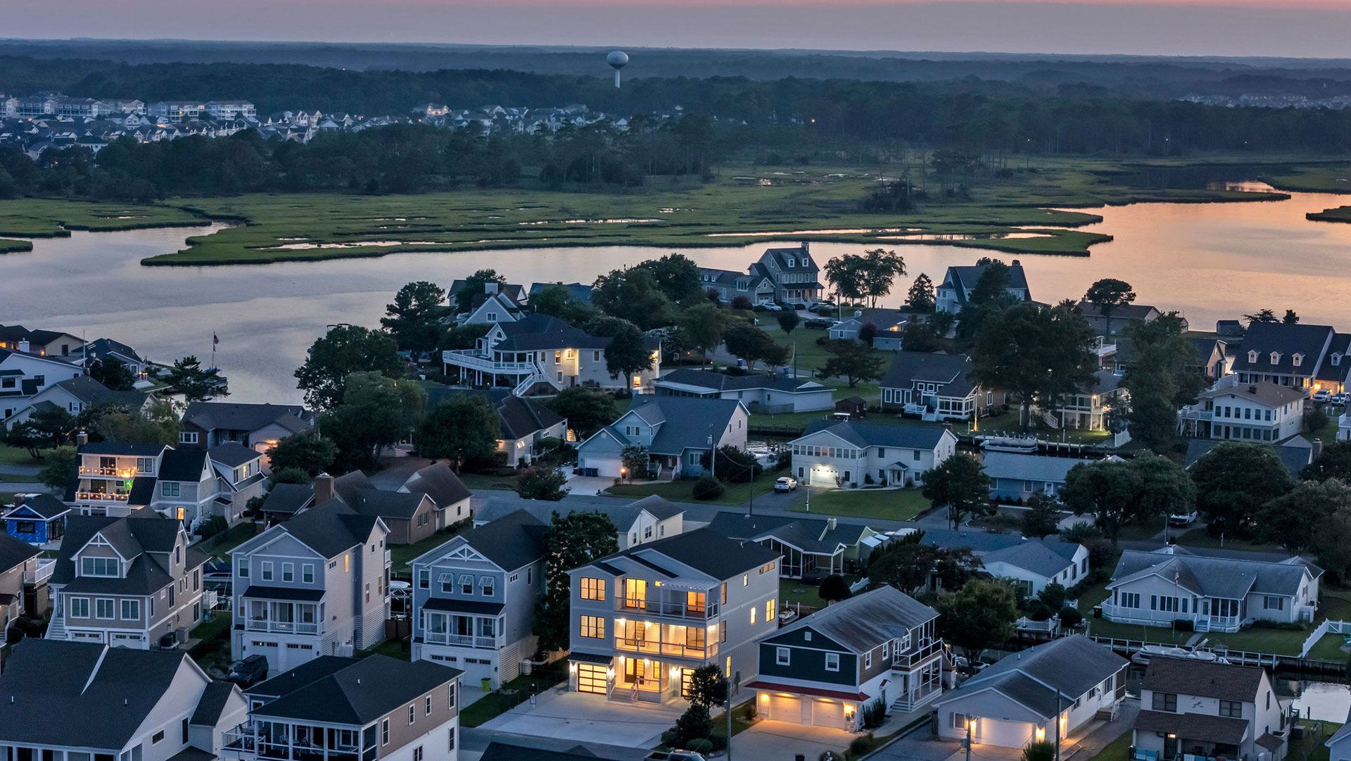 Aerial view of coastal houses at dusk, with a lake and marsh in the background.