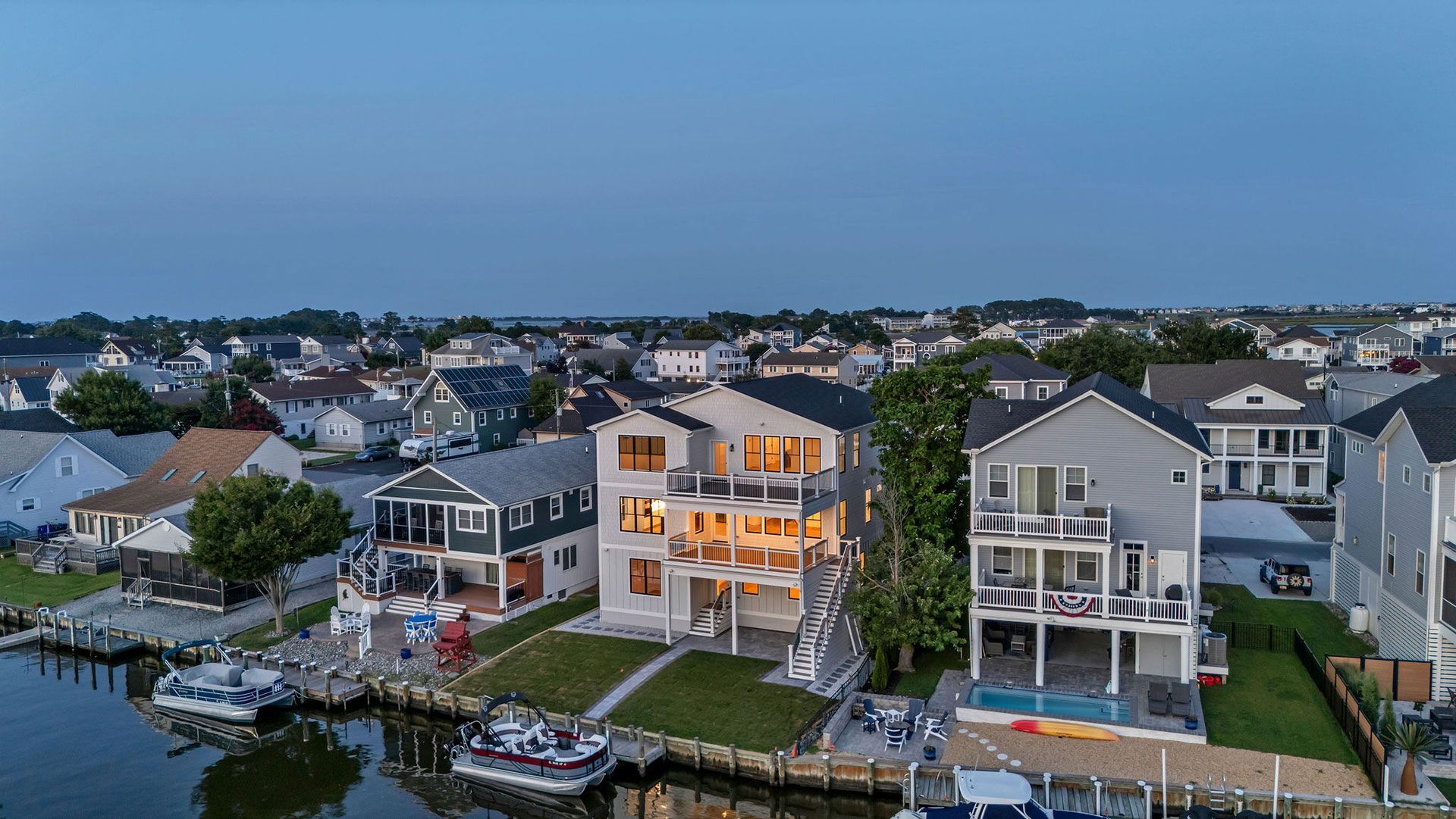 Aerial view of waterfront homes at dusk, with boats docked and surrounding neighborhood.
