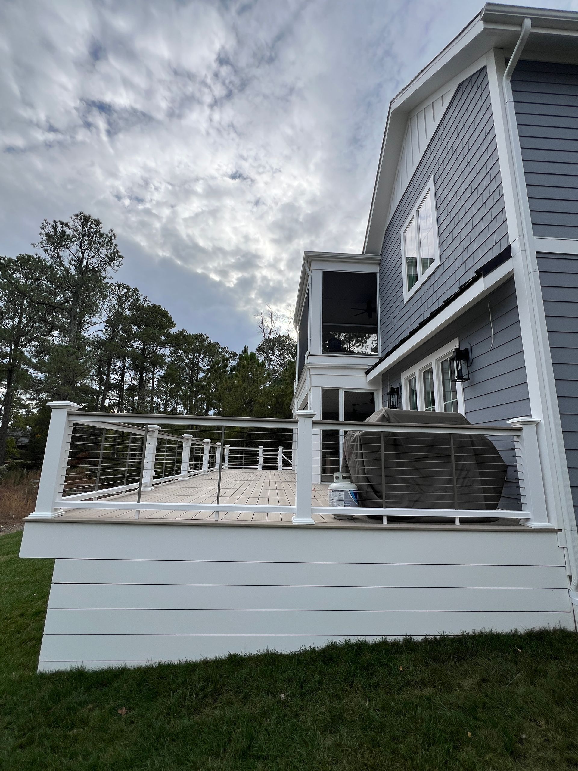 A gray house with a white deck and a grill on it.