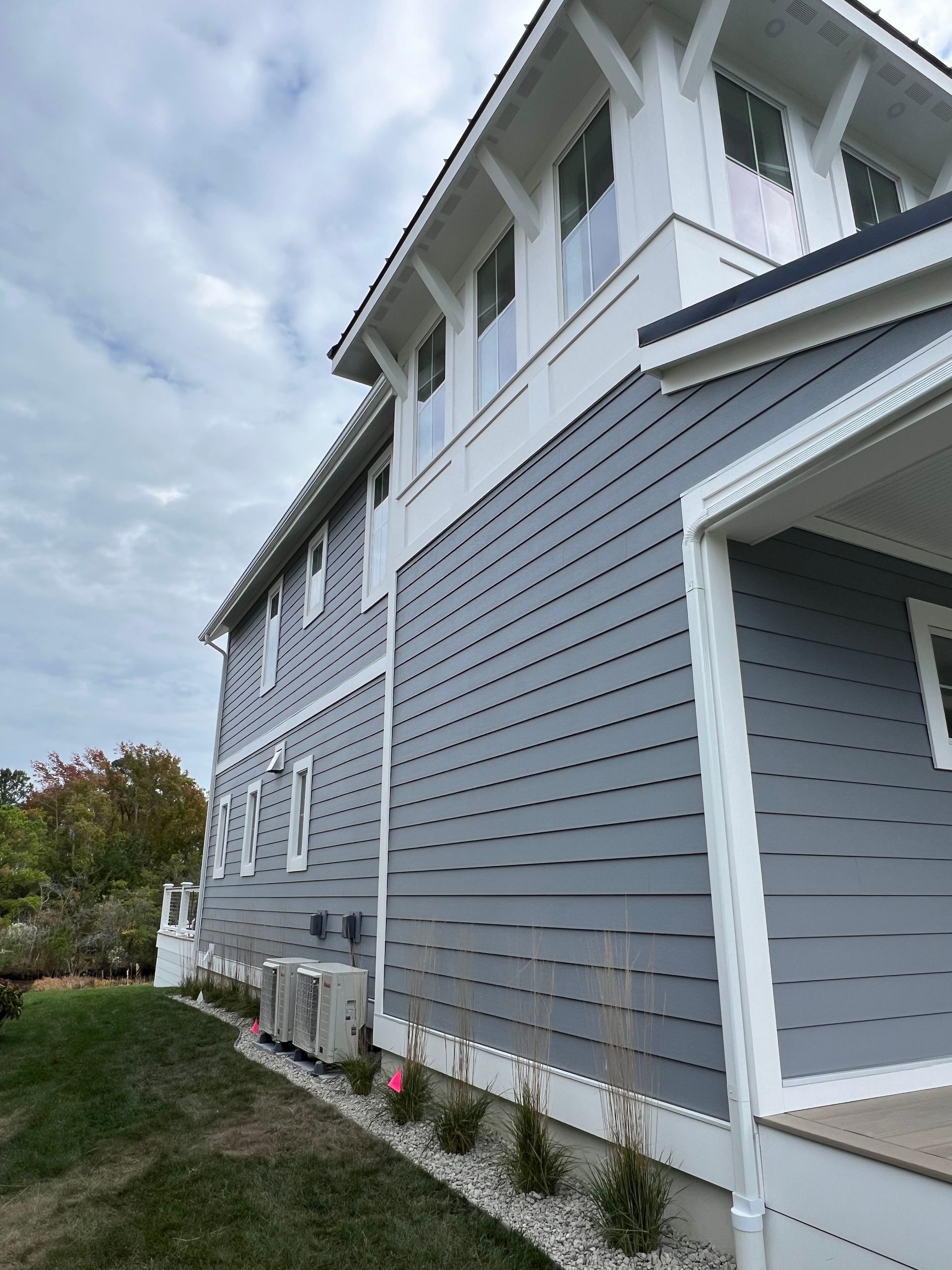 A large house with a gray siding and white trim is sitting on top of a lush green lawn.