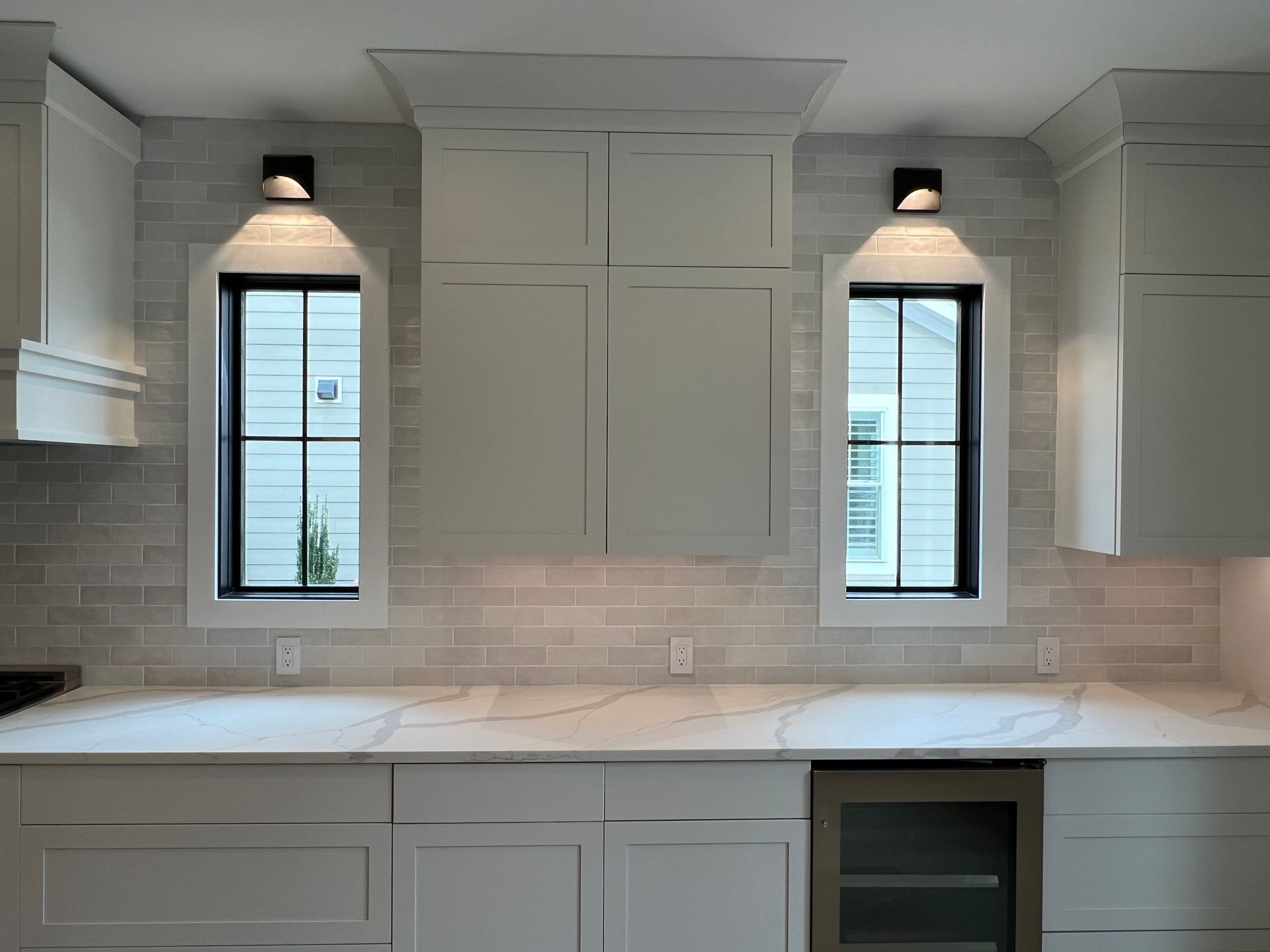 A kitchen with white cabinets and two windows.