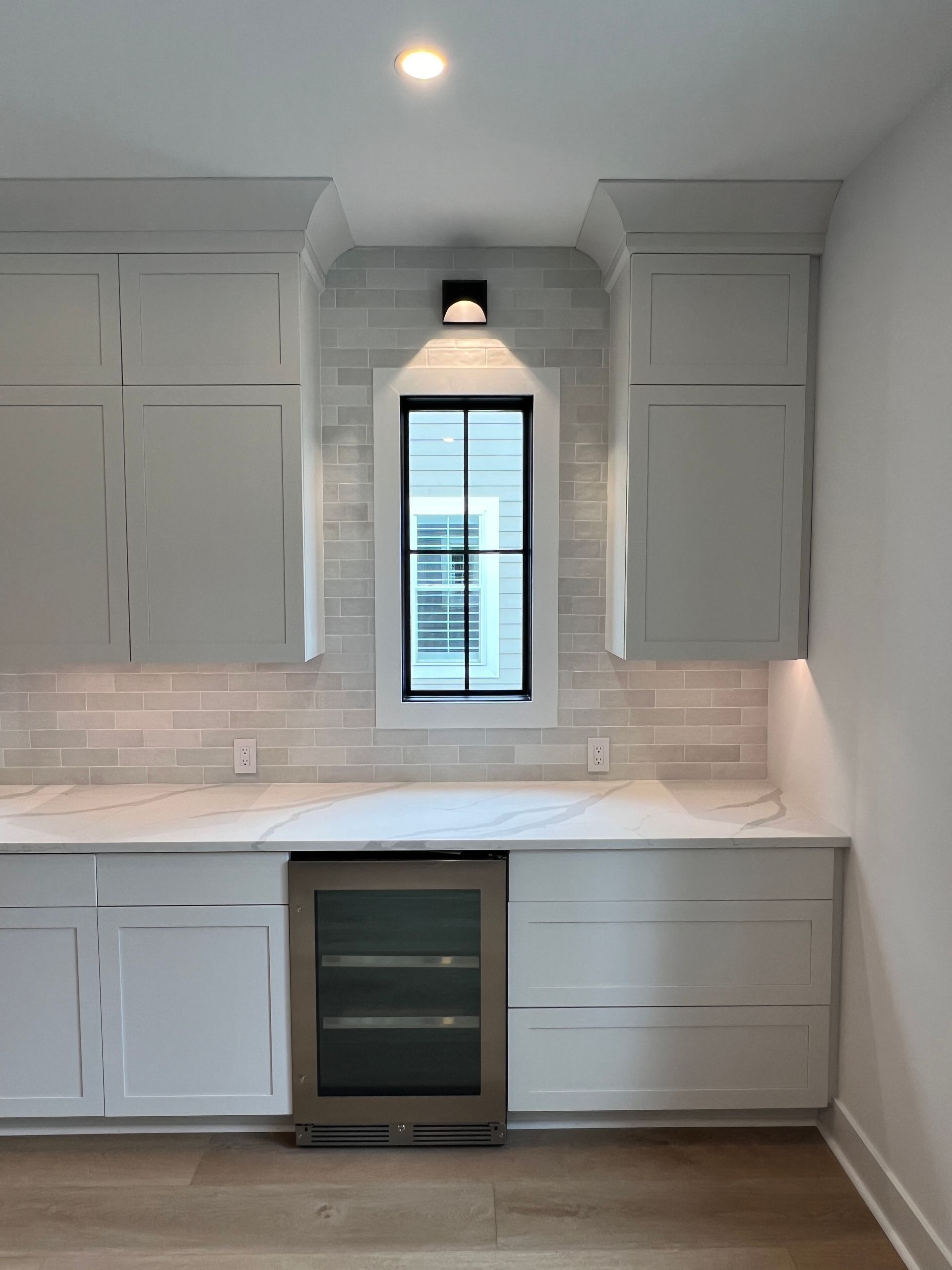 A kitchen with white cabinets , a refrigerator and a window.