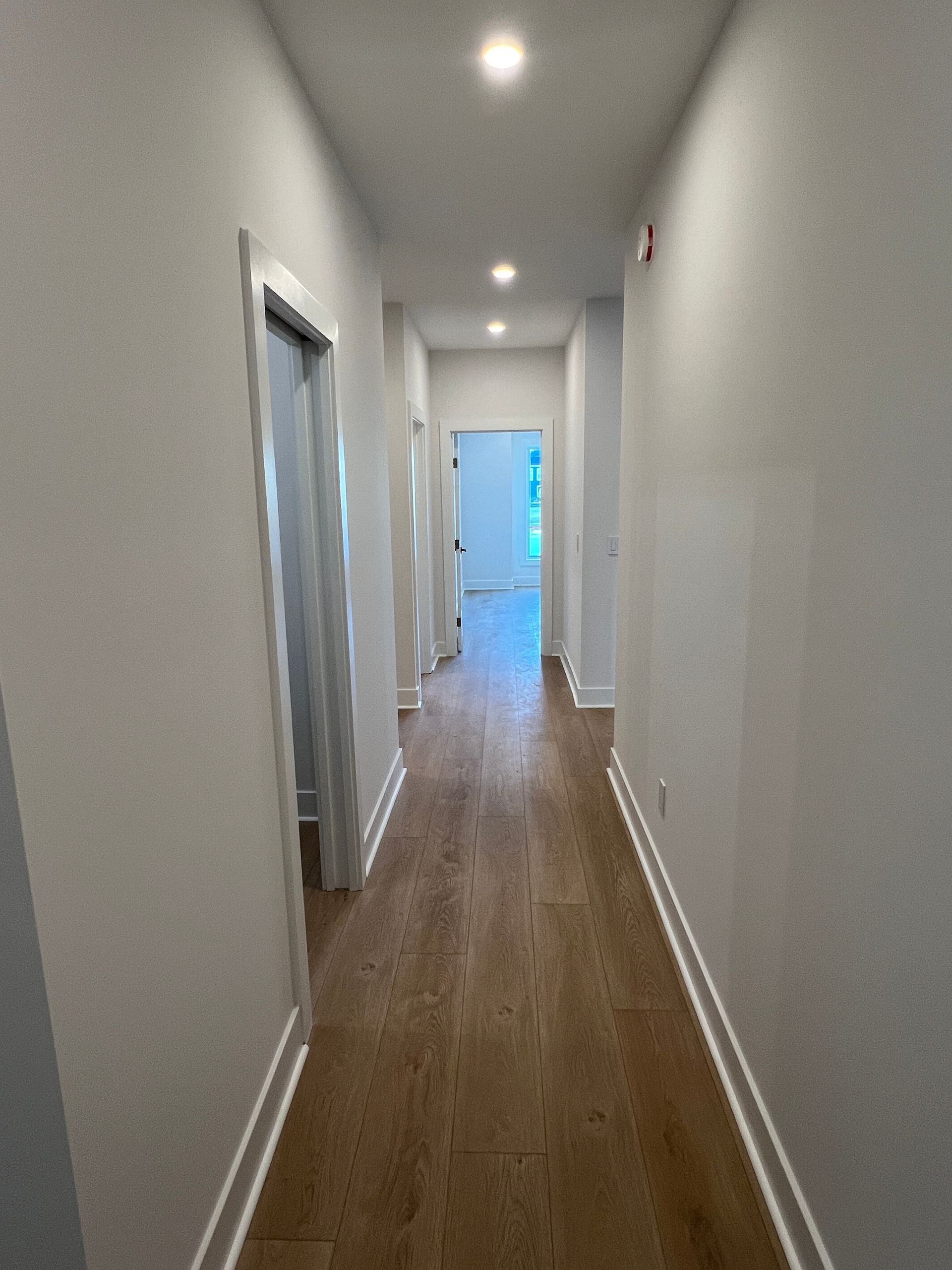A long hallway with wooden floors and white walls in a house.