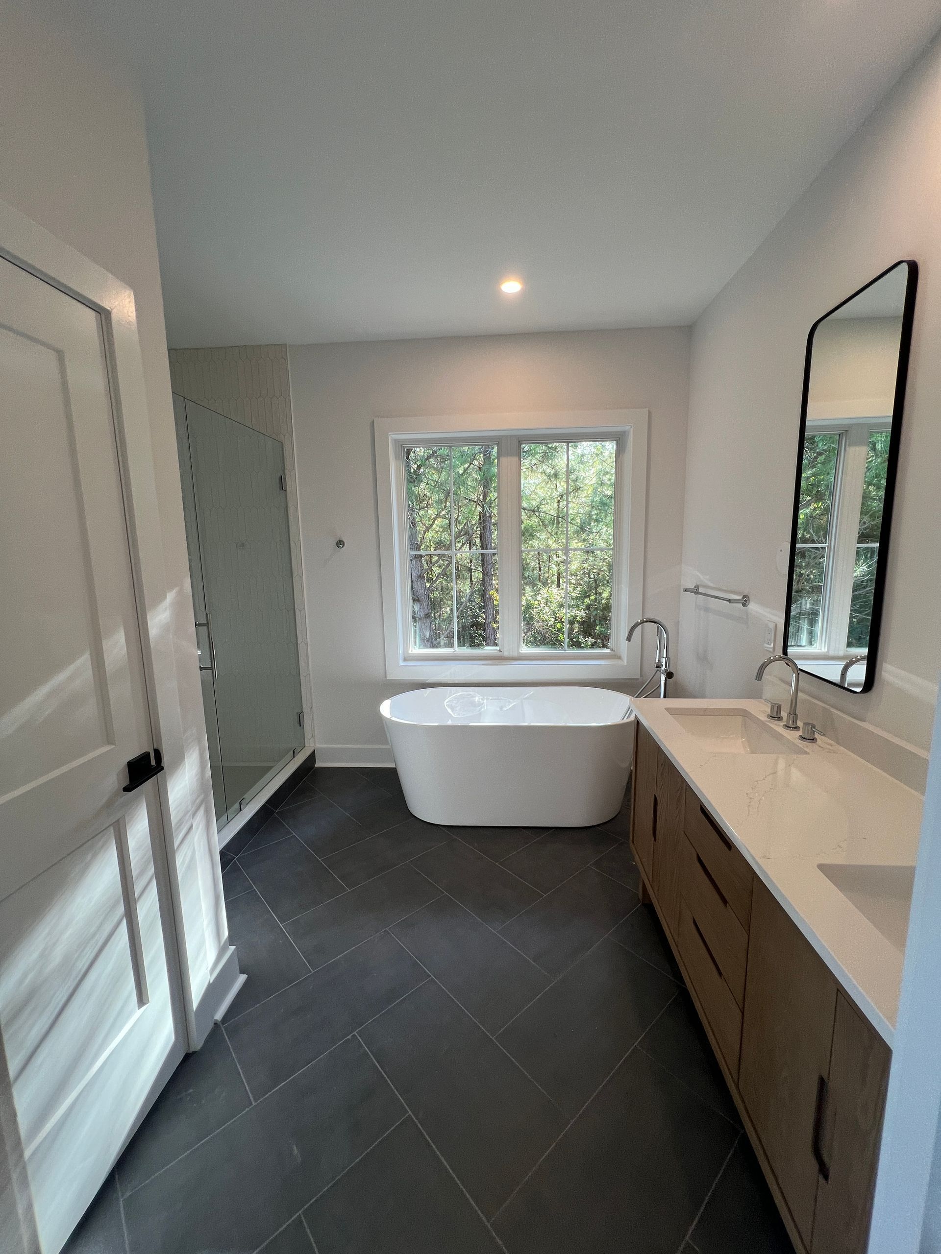 A bathroom with a tub , sink , mirror and window.