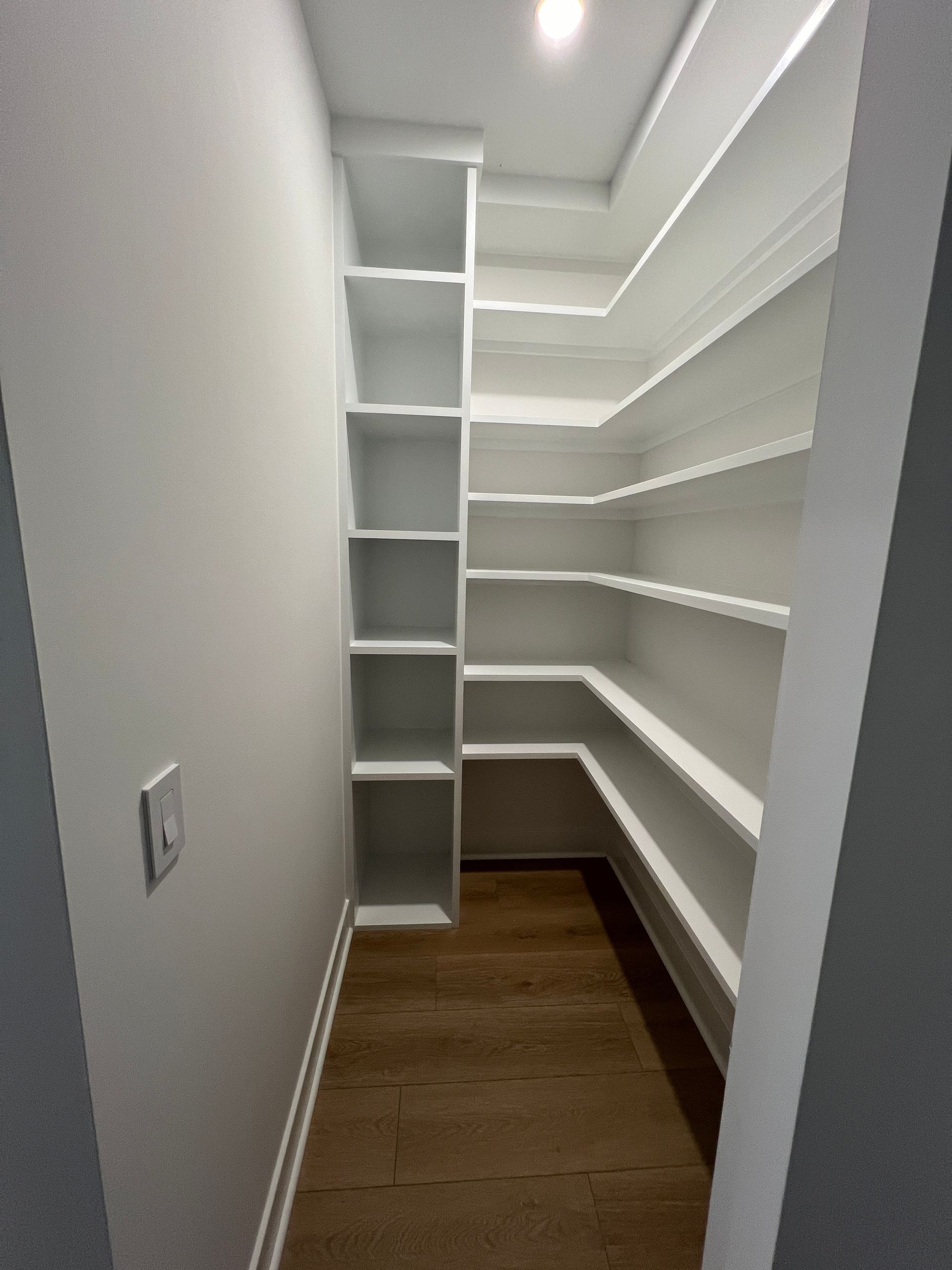 A walk in closet with white shelves and wooden floors.