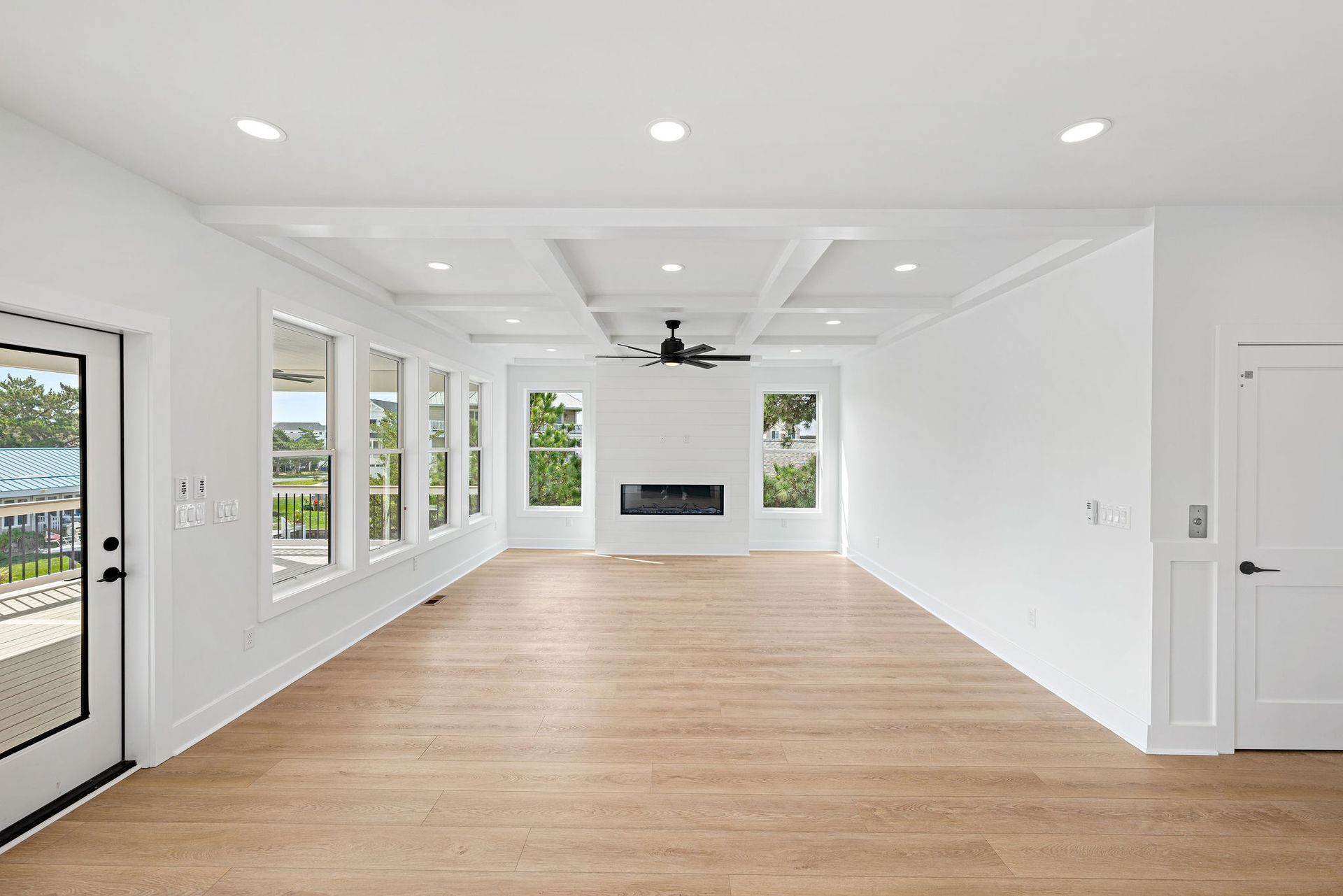 An empty living room with hardwood floors , white walls and a fireplace.