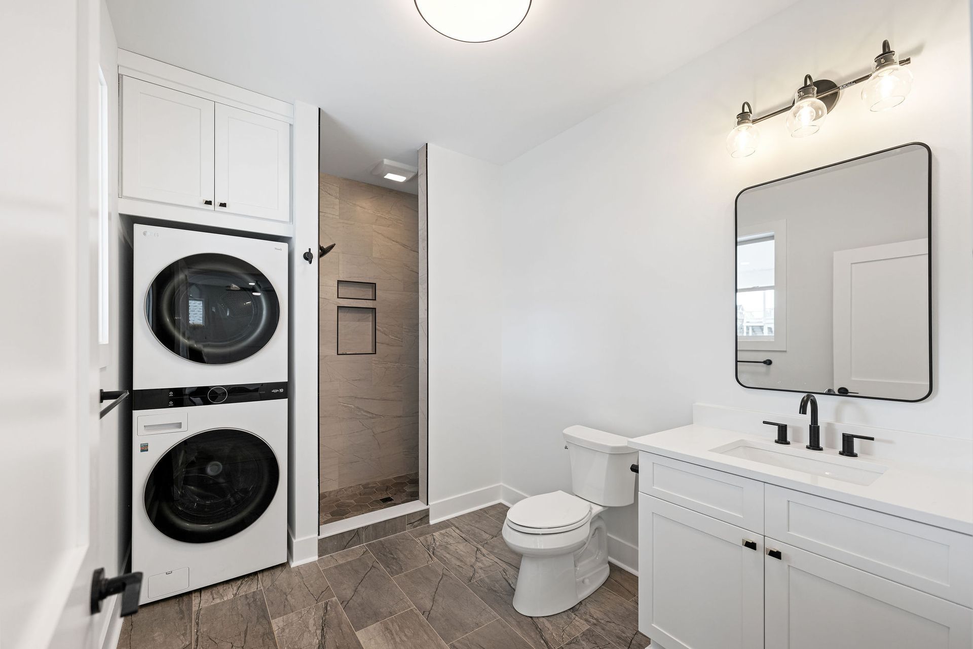 A bathroom with a washer and dryer stacked on top of each other and a toilet.