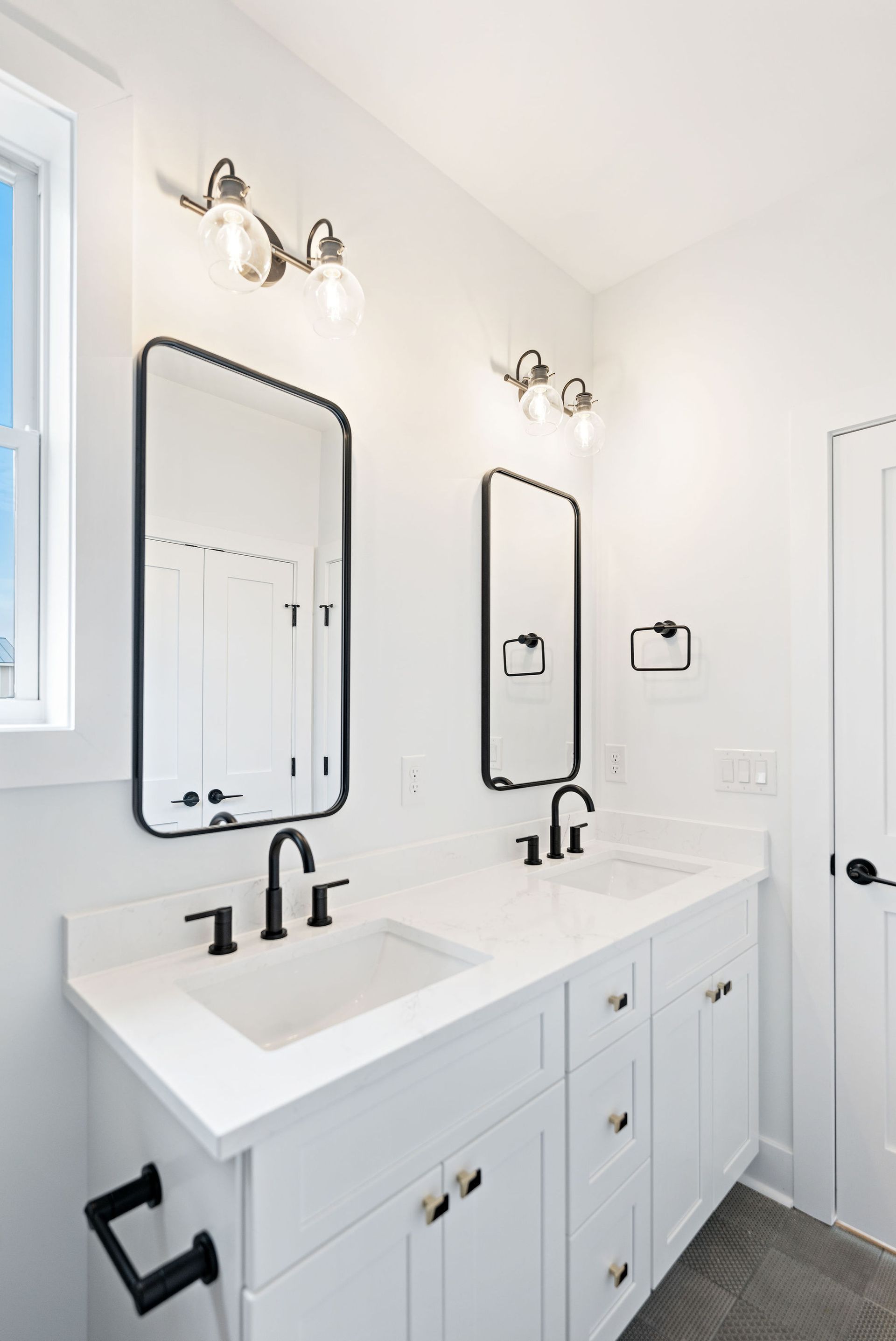 A bathroom with two sinks , two mirrors and a window.