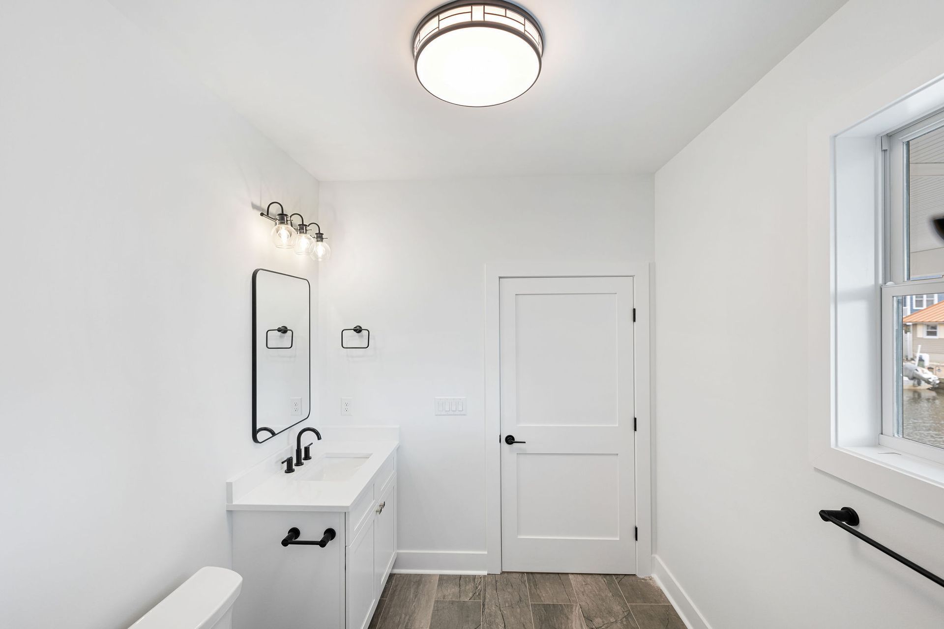 A bathroom with a sink, toilet, mirror and window.