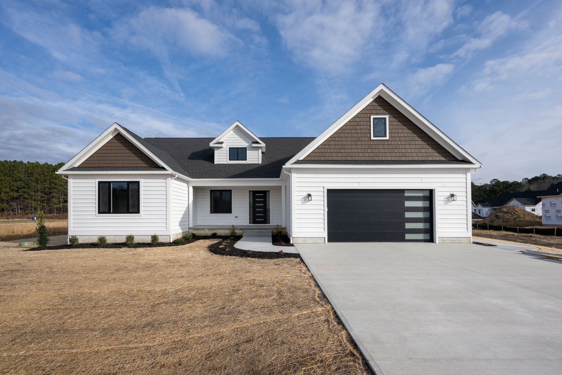New white house with black roof, attached garage, and concrete driveway under a blue sky