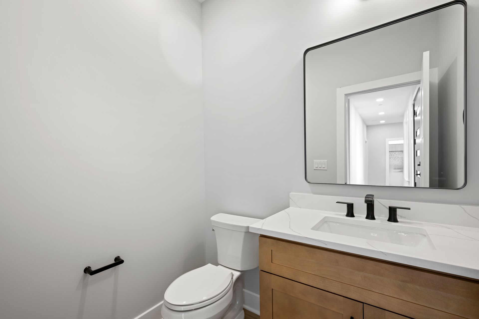 Modern bathroom with white walls, wooden vanity, toilet, and large wall mirror