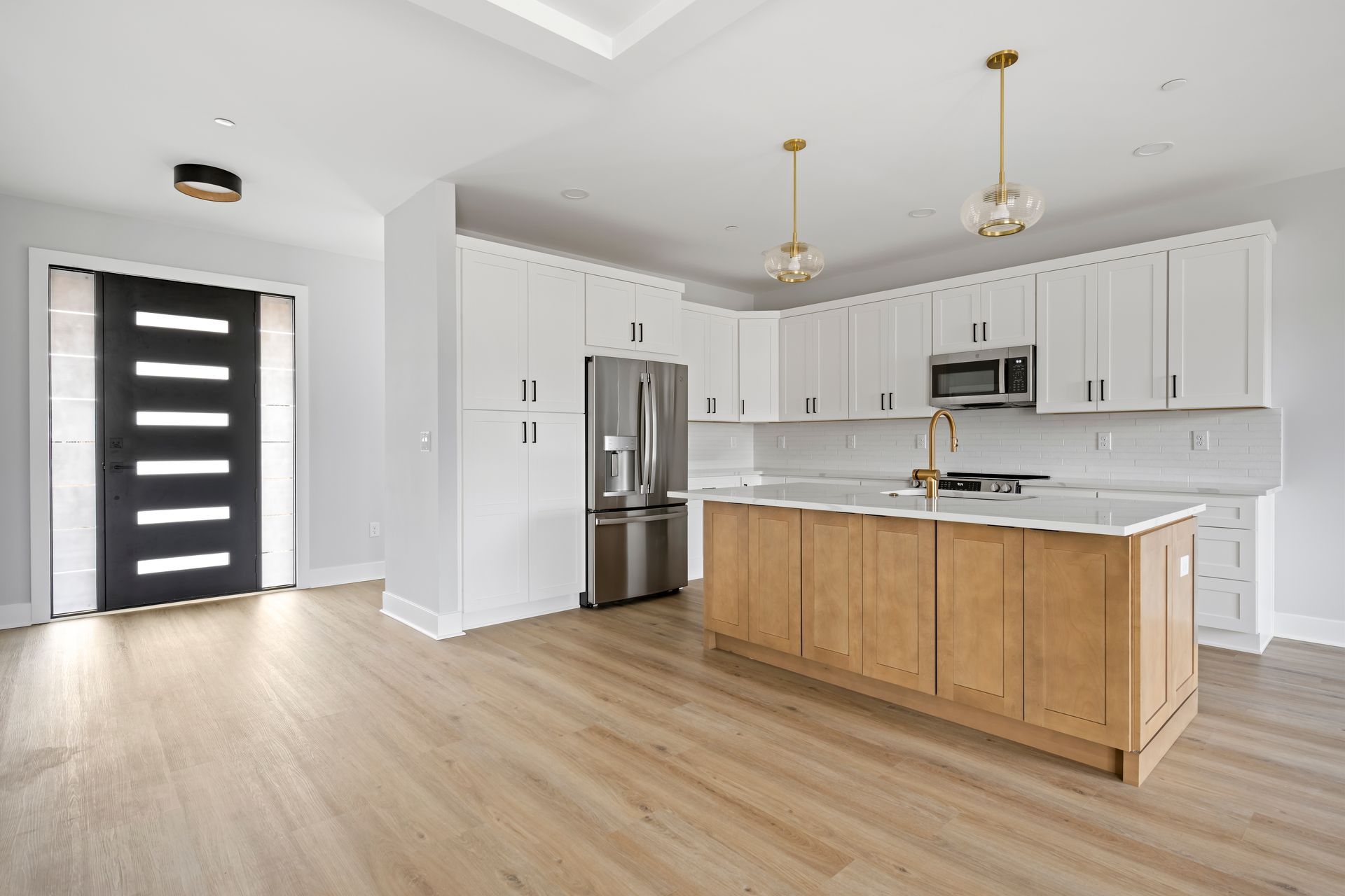 Bright modern kitchen with white cabinets, stainless appliances, and a wood island near a black front door