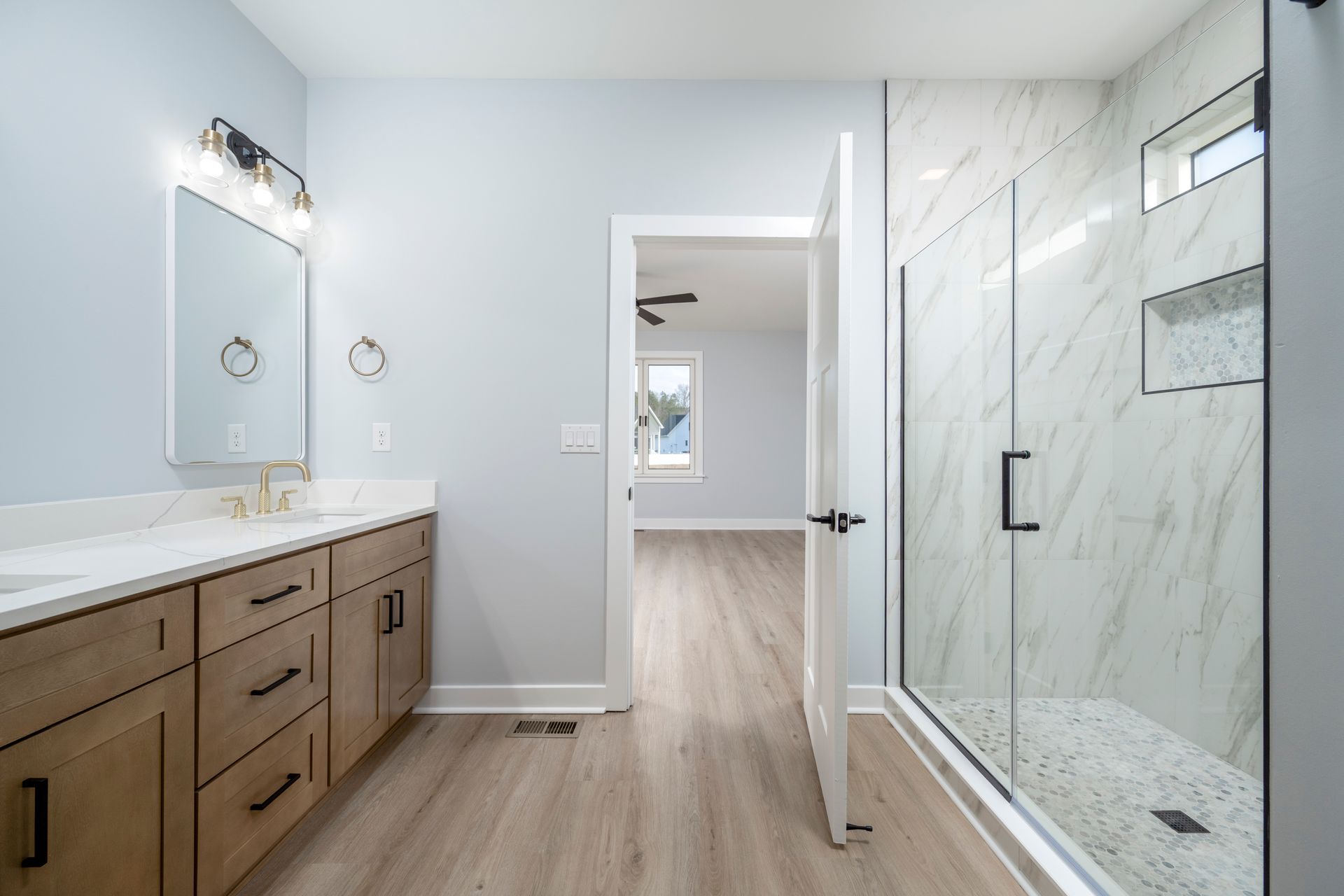 Modern bathroom with double vanity, glass shower, and open door to adjacent room