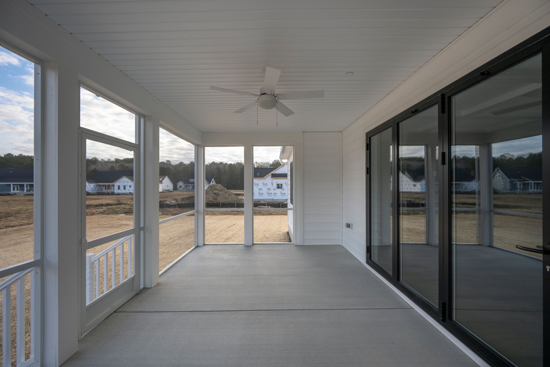Covered back porch with white ceiling fan, concrete floor, screened windows, and sliding glass doors.