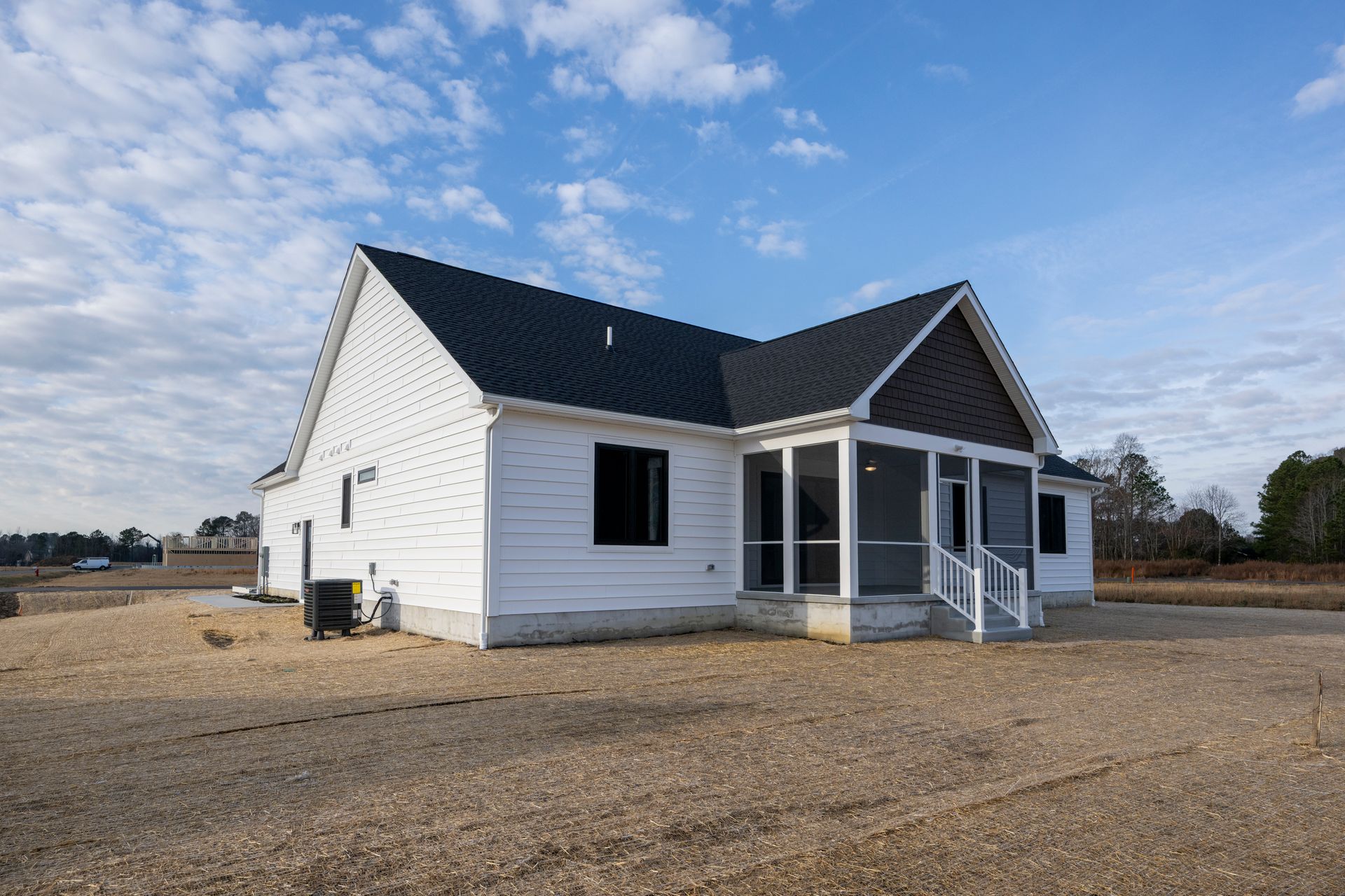 White single-story house with a dark roof and front porch on a gravel lot under a blue sky