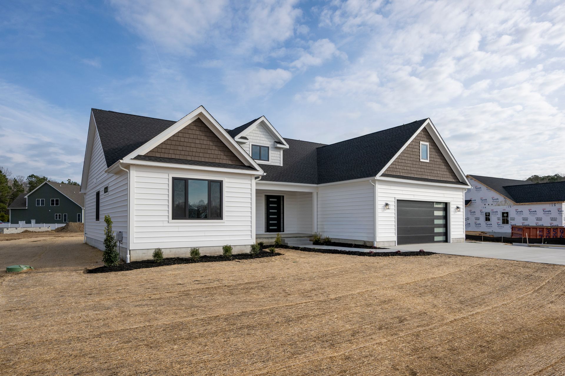 New white house with black roof and attached garage on a bare lot under a blue sky