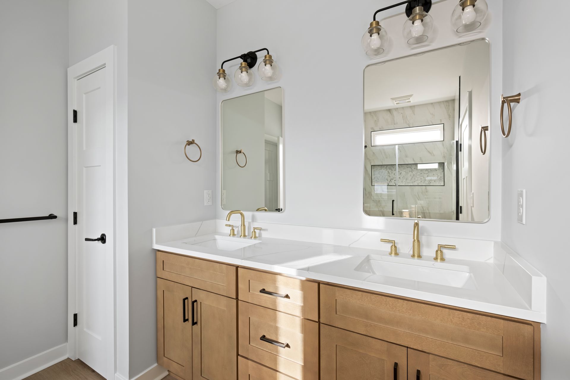 Modern bathroom double vanity with wood cabinets, white countertops, gold fixtures, and framed mirrors
