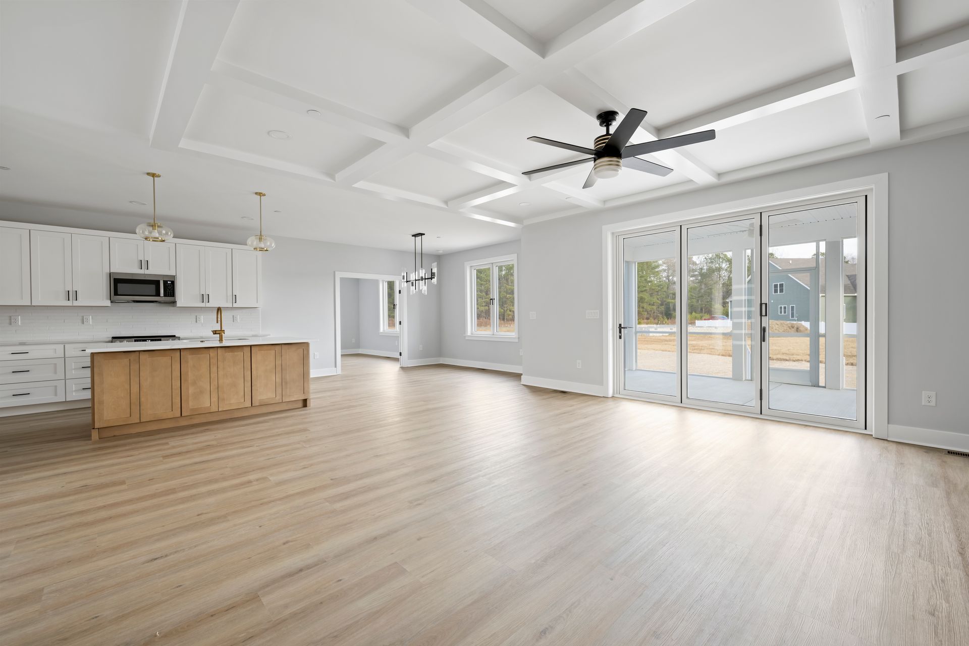 Bright open-concept living room with white walls, light wood floors, kitchen island, ceiling fan, and sliding glass doors