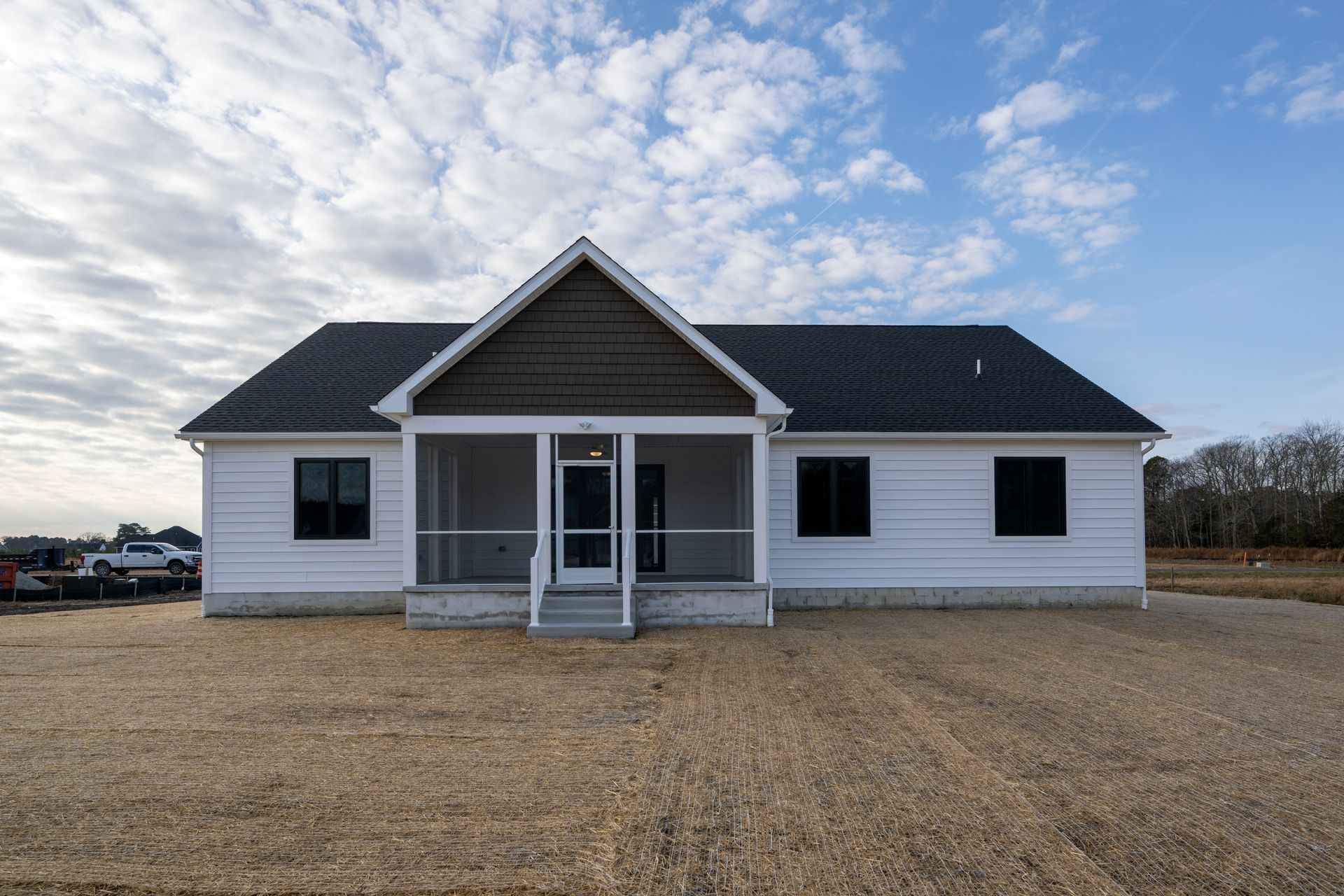 White single-story house with dark roof and front porch on a gravel lot under a partly cloudy sky