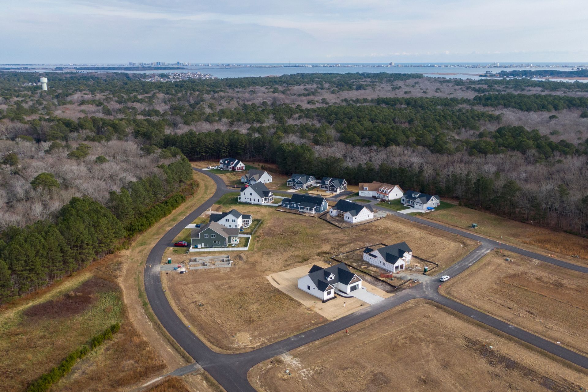 Aerial view of a suburban housing development with roads, vacant lots, and surrounding trees.