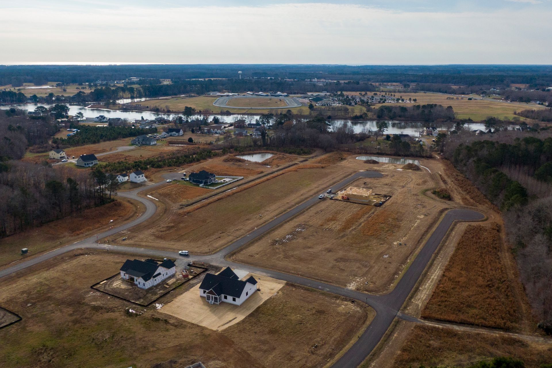 Aerial view of a suburban housing development with roads, lots, and open land under a cloudy sky