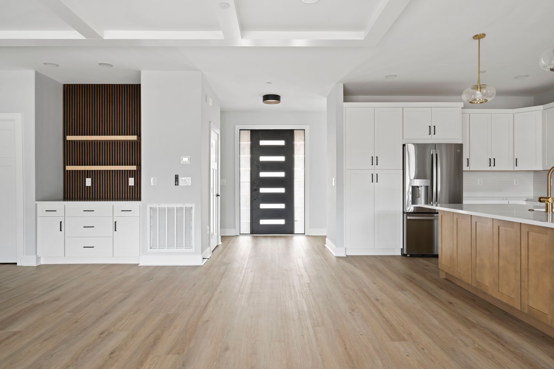 Bright modern empty kitchen and living area with wood floors, white cabinets, and stainless steel appliances