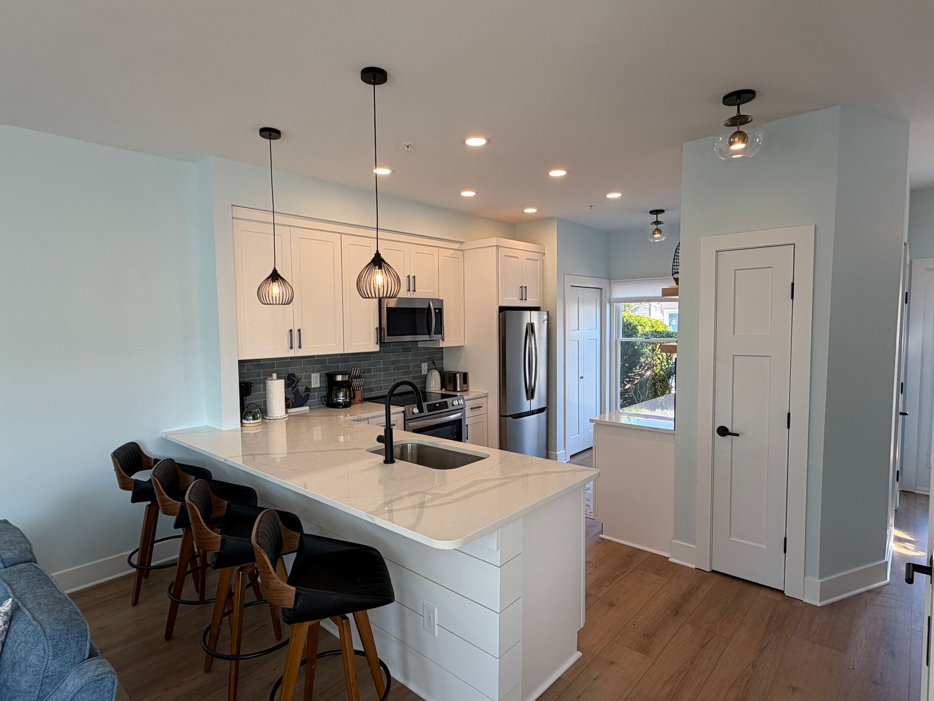 Modern white kitchen with island, pendant lights, wood floors, and stainless steel refrigerator