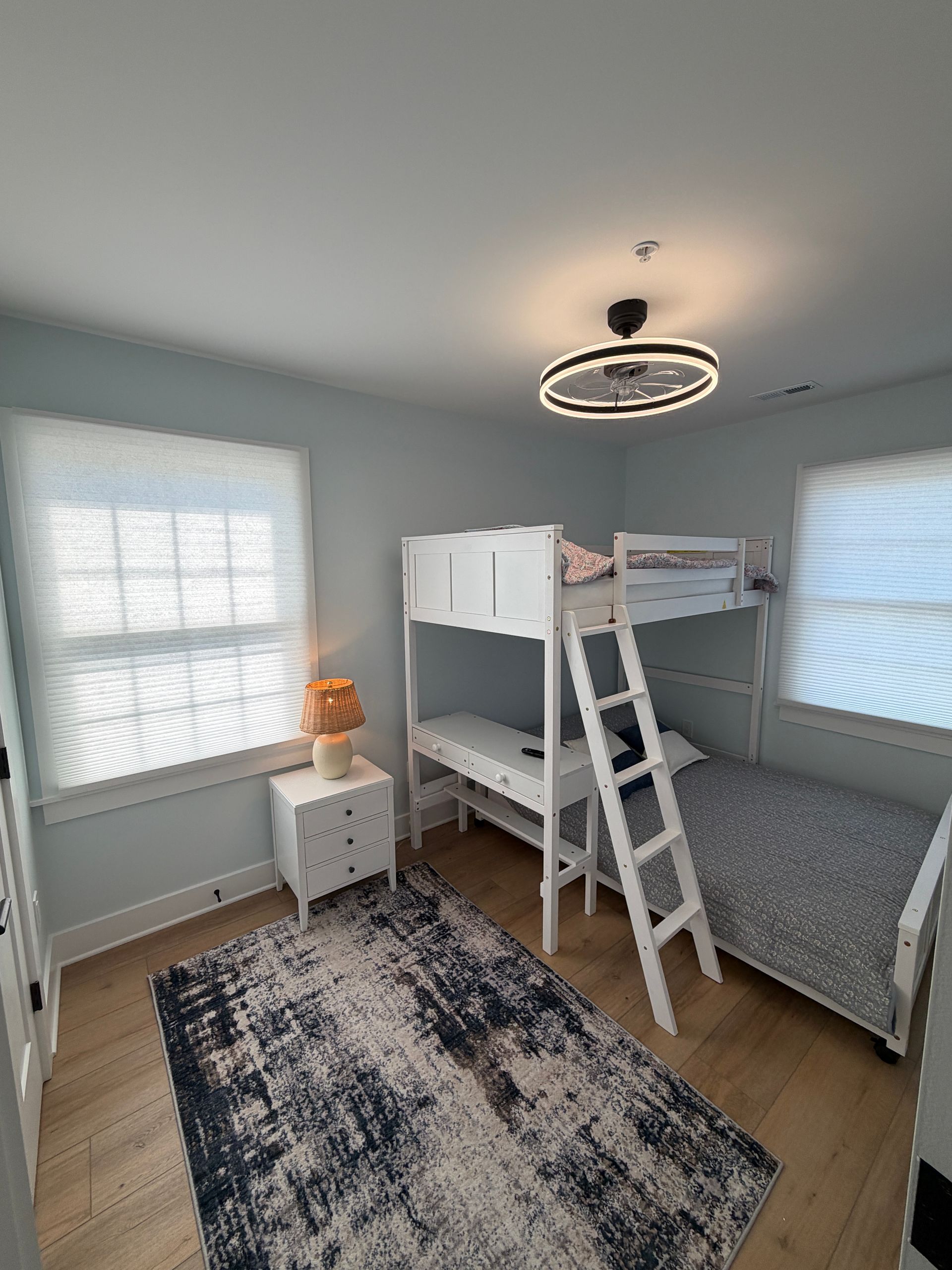 Small empty room with light blue walls, wood floor, and two windows viewed from the doorway