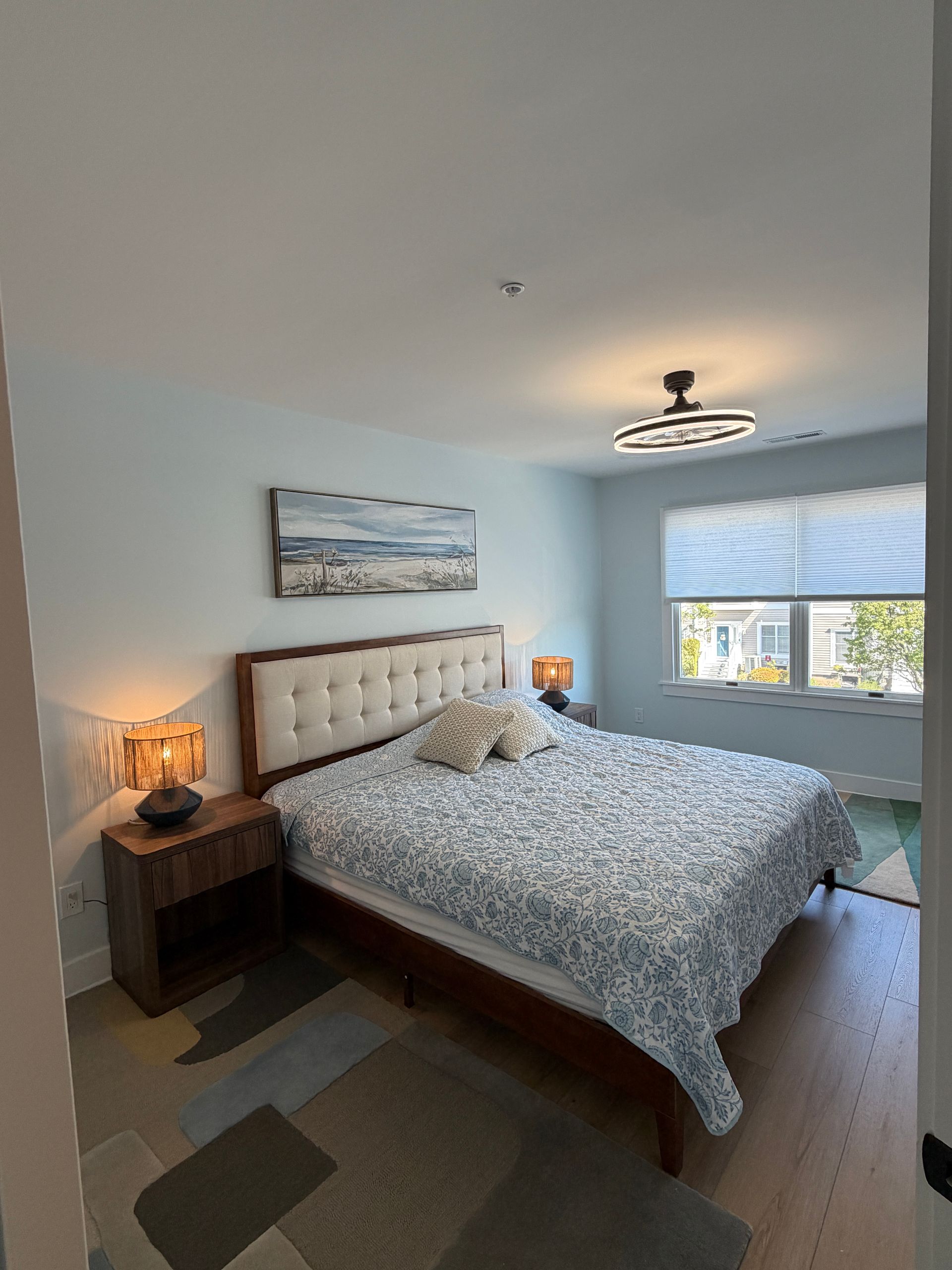 Empty room with light wood floors, white walls, and a window overlooking houses outside.