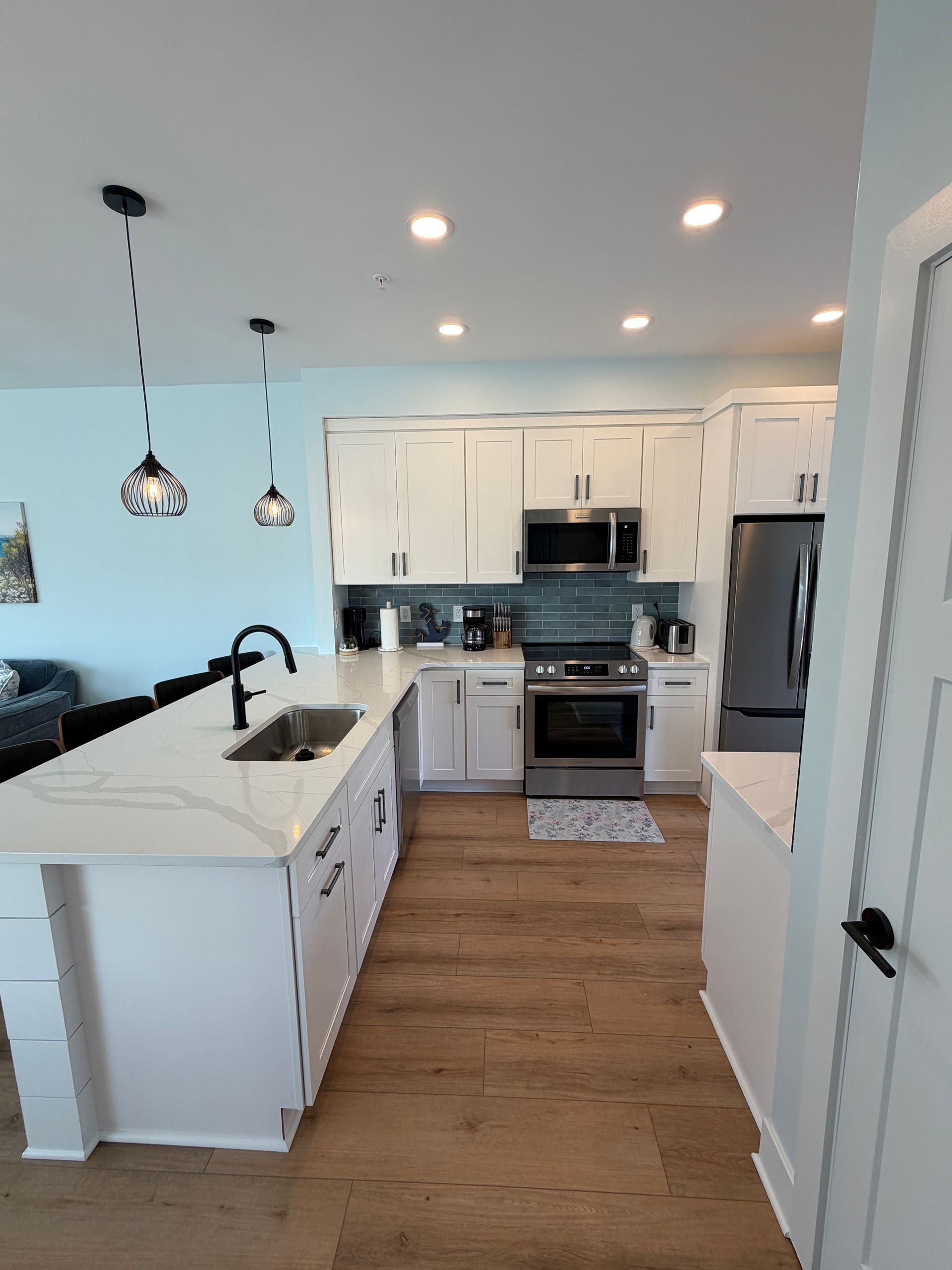 Bright modern kitchen with white cabinets, island, stainless appliances, and wood floors