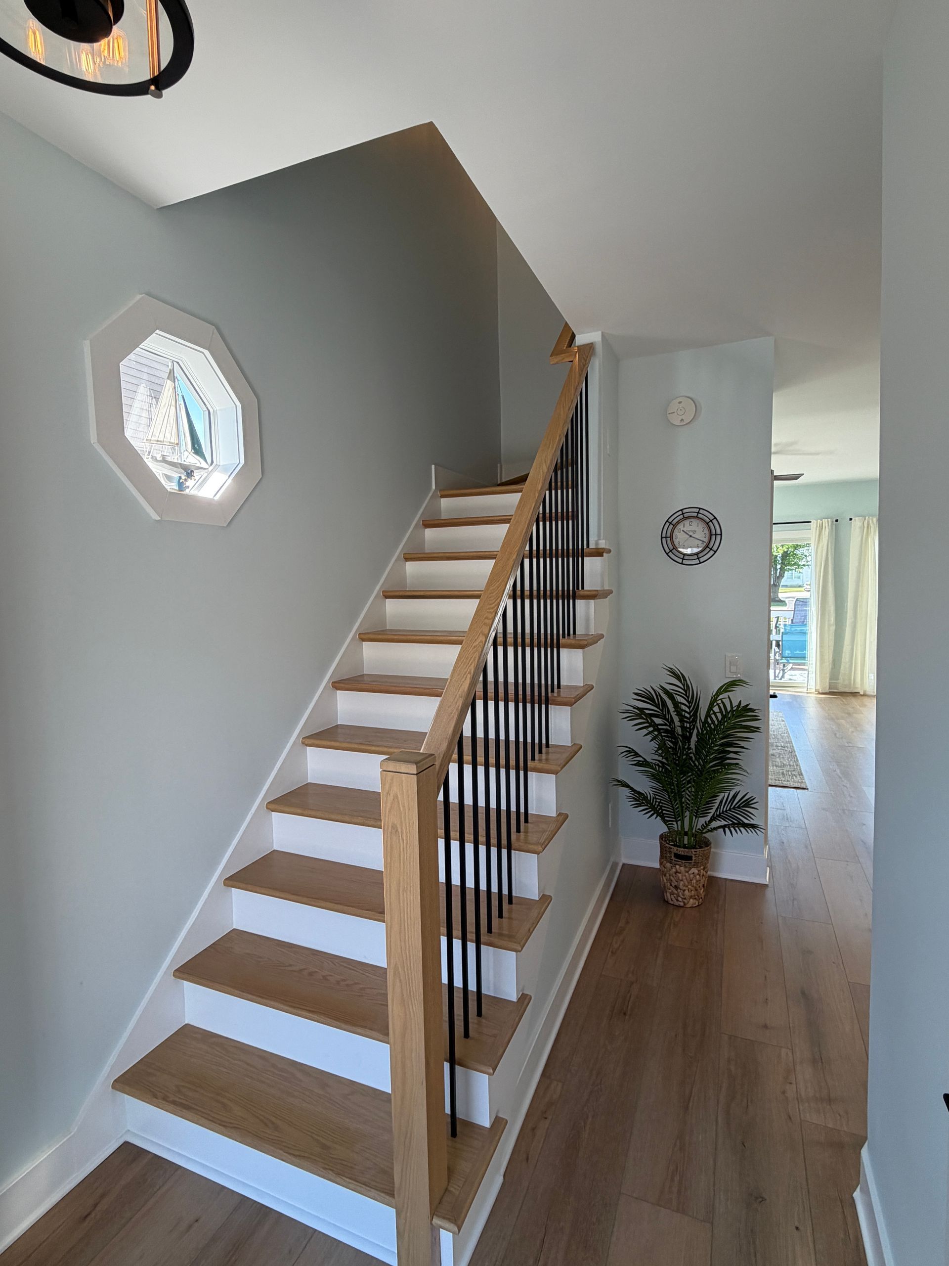 Interior entryway with a staircase, white walls, wood floors, and a small octagonal window.
