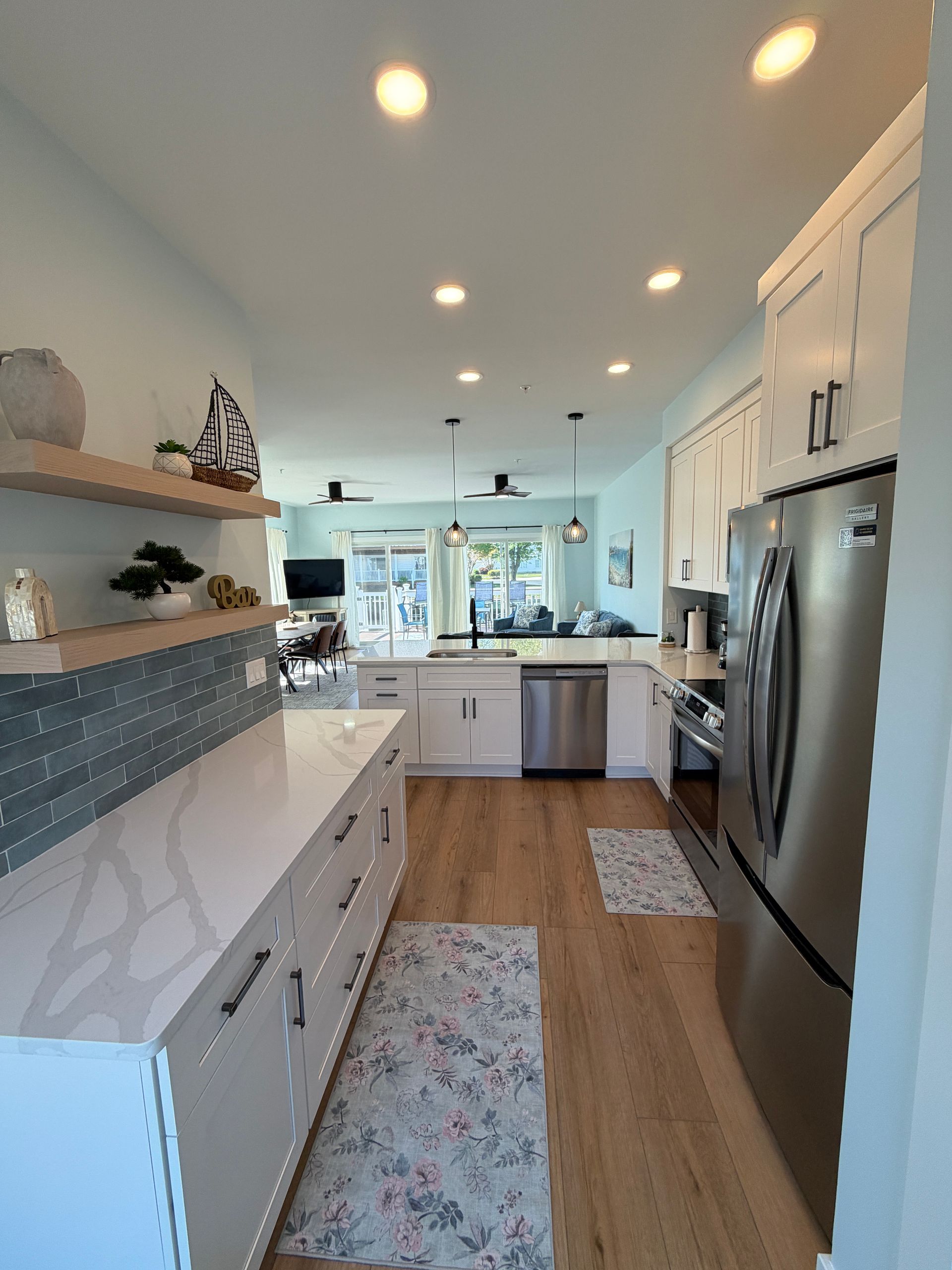 Modern kitchen with white cabinets, wood floors, stainless refrigerator, and floating shelves