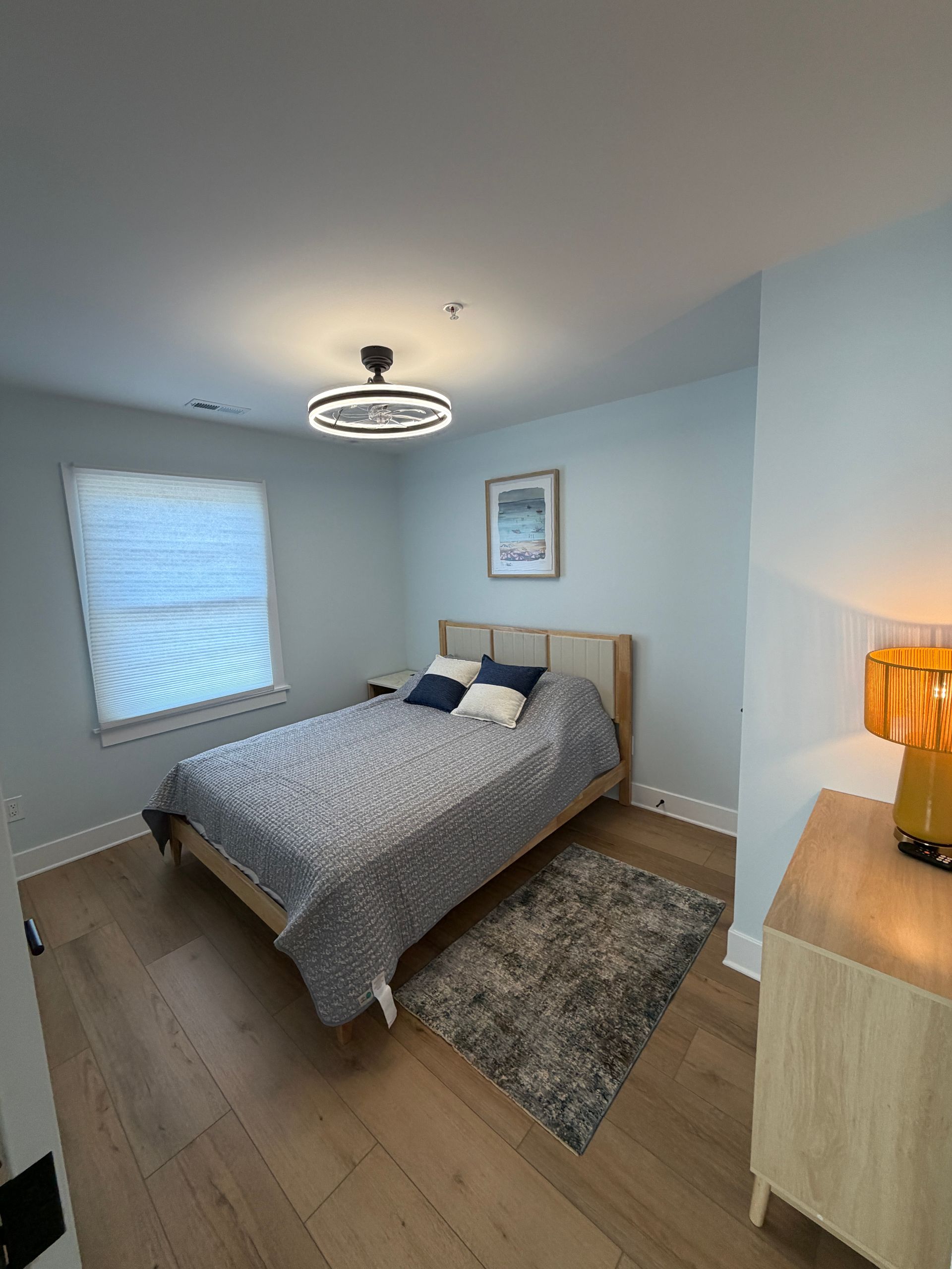 Empty light-blue bedroom with wood floors, a window, and a black ceiling light.