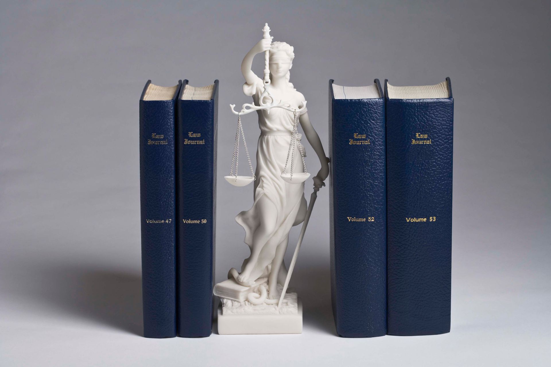 A statue of lady justice standing next to three books