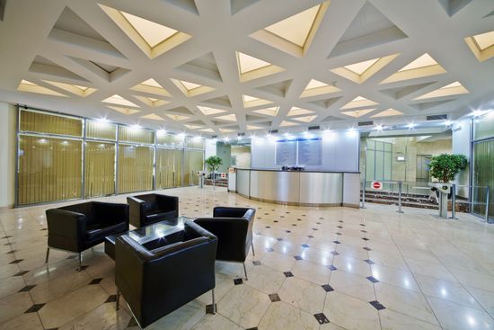 Modern office lobby with black seating, a reception desk, and geometric ceiling lights.