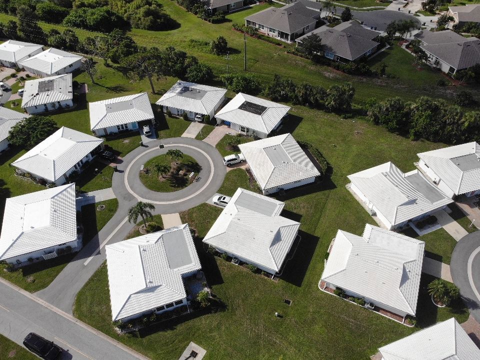 Aerial view of houses with white roofs surrounding a roundabout on green grass.