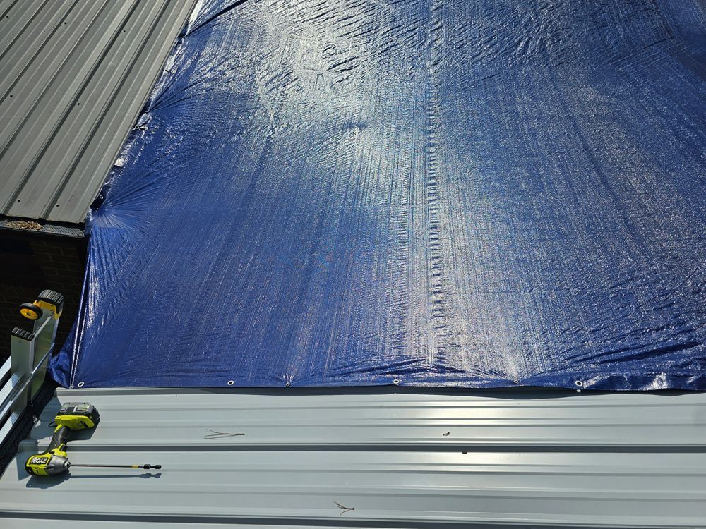 Blue tarp covering a metal roof, tools on the edge.