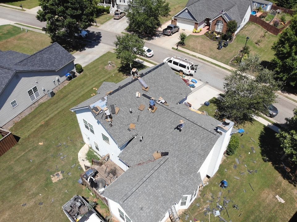 Roofers working on a residential roof, tools and materials visible. Suburban setting, sunny day.