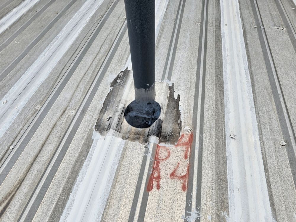 A black pipe rising from a metal roof, sealed with white sealant, next to a red 