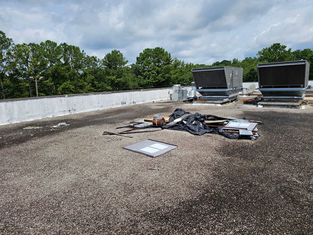 Rooftop with debris, two HVAC units, and trees in background under a cloudy sky.