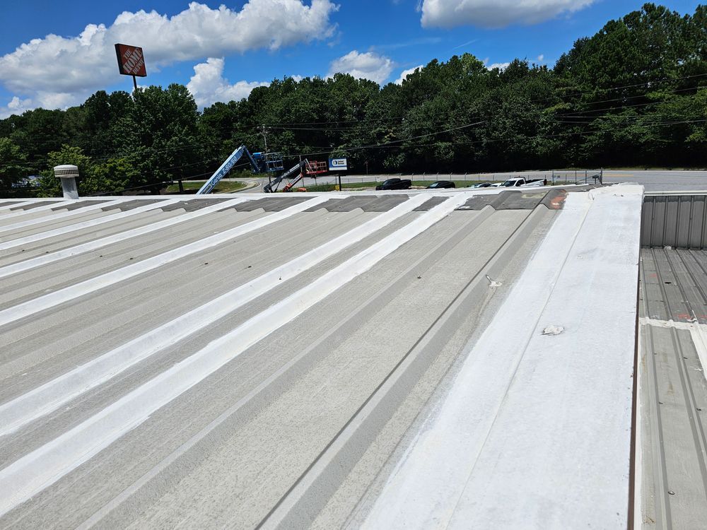 Metal roof of a building with white-painted ridges, under a bright blue sky. A sign and trees are in the background.
