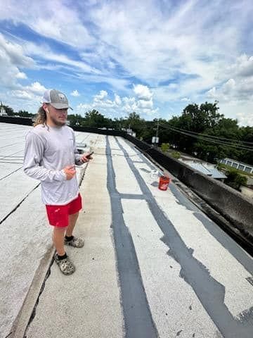 Man on a flat roof with painted lines, wearing a long-sleeve shirt, shorts, and a hat; sunny sky.