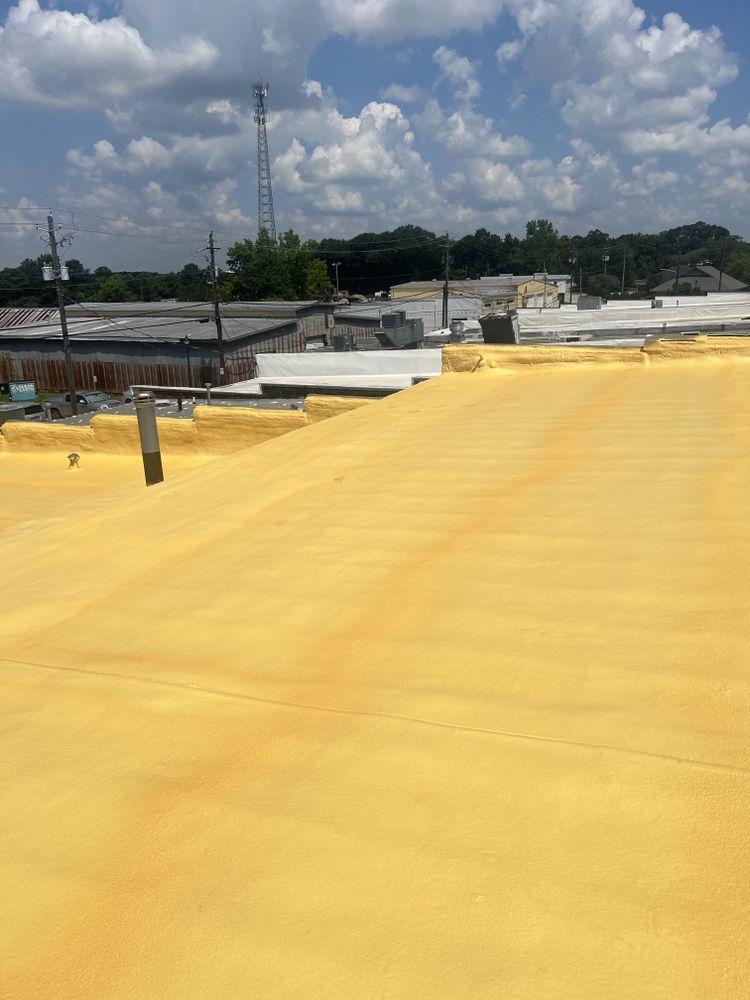 Yellow-coated roof under a blue sky with clouds; industrial setting, possibly after foam insulation application.