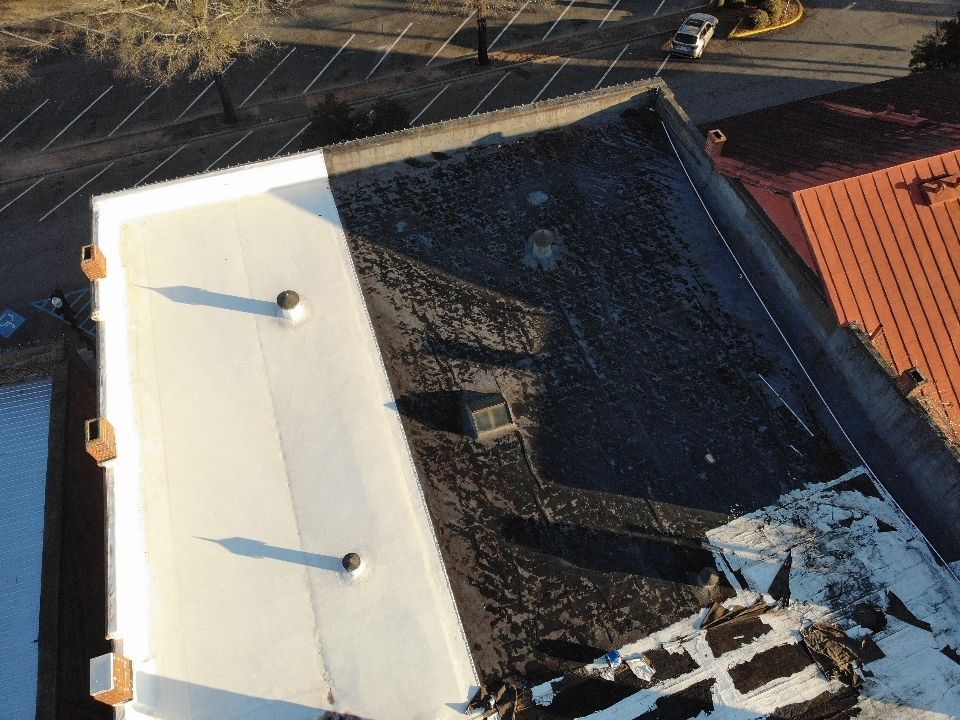 Overhead view of a building roof, half white and half dark, with a parking lot visible in the background.